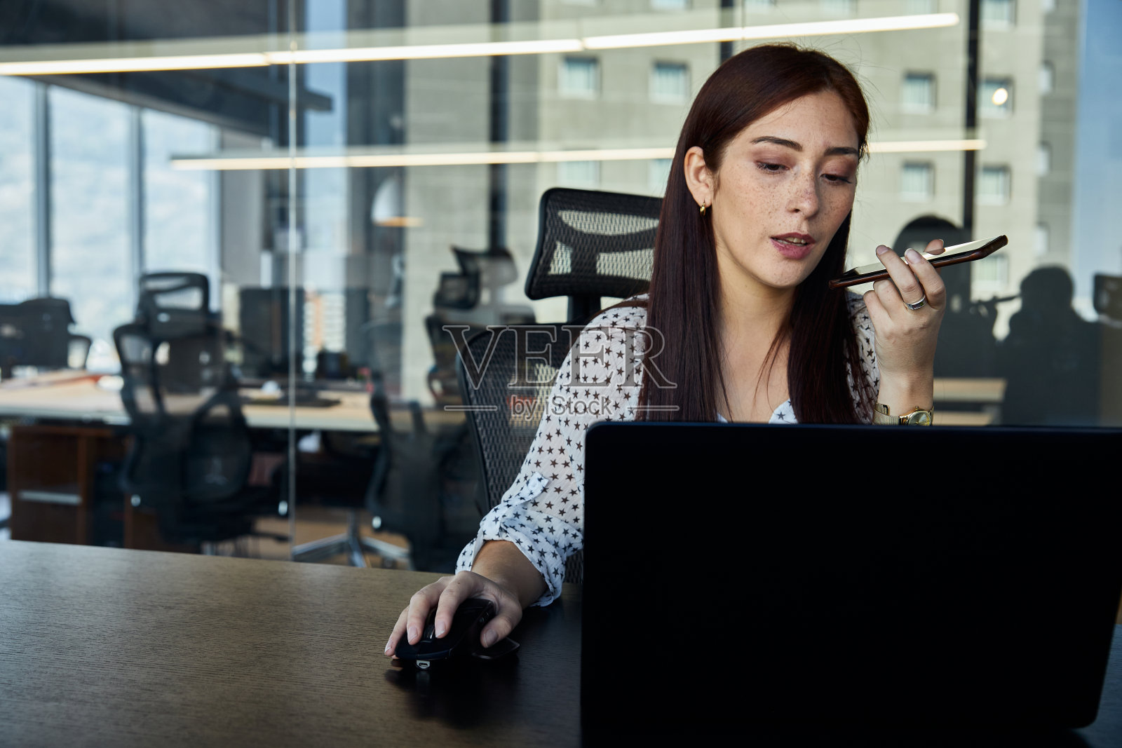 年轻、美丽、强大的女性企业家，在会议办公室里一边用智能手机开着免提，一边用笔记本电脑工作照片摄影图片