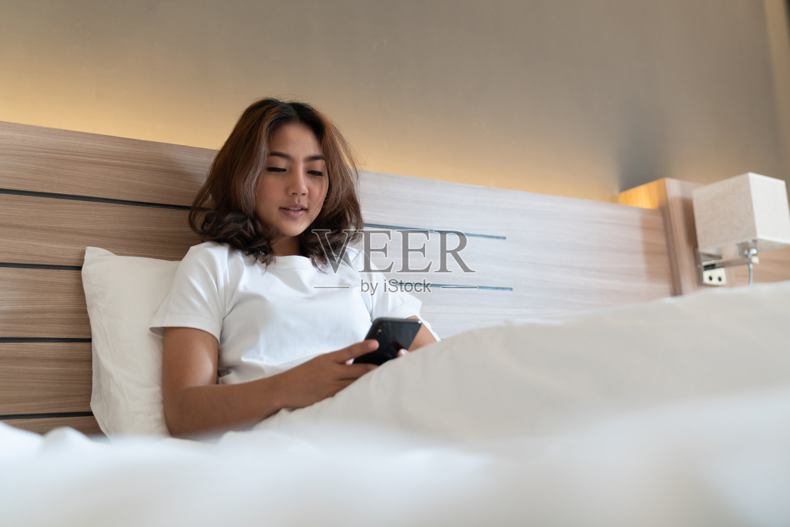 年轻的亚洲女性躺在床上发短信，用智能手机查看社交应用照片摄影图片