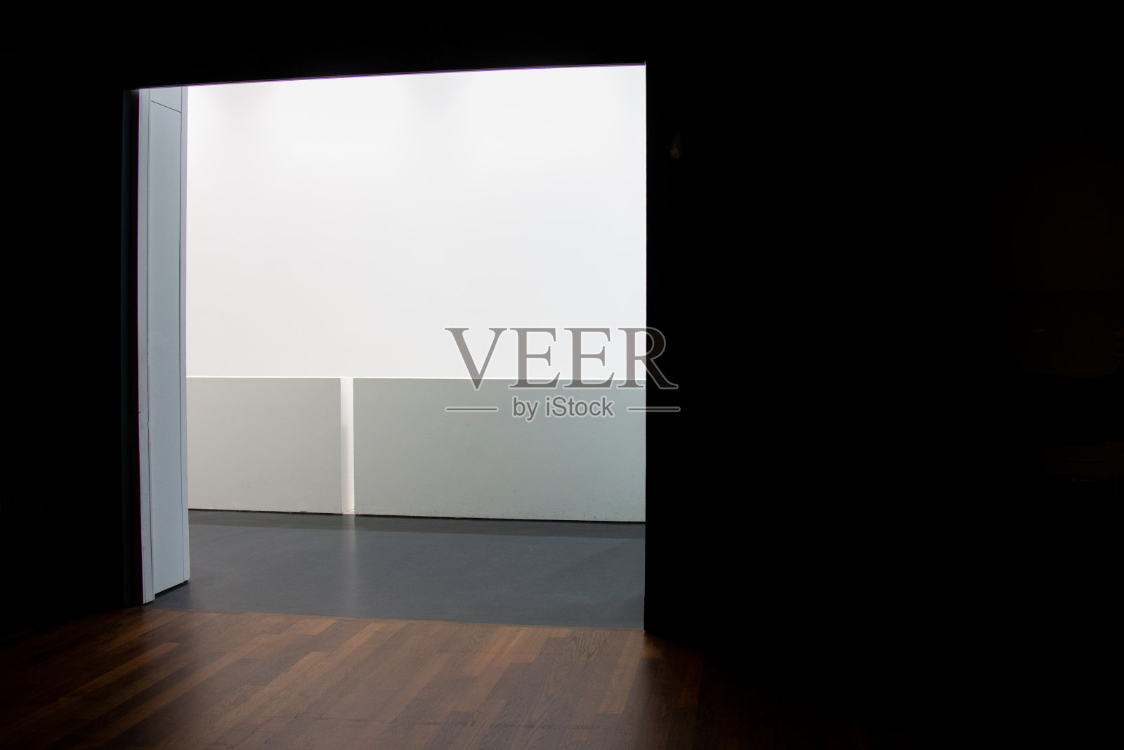 从一个黑暗的房间与黑色墙壁和木质拼花到一个明亮的房间与白色墙壁和灰色墙板-复制空间照片摄影图片