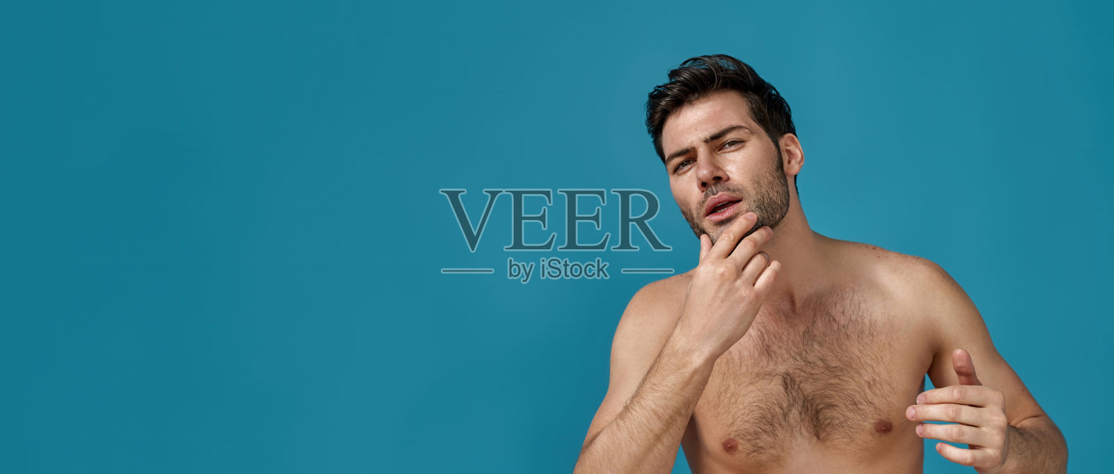 有吸引力的自信的棕色头发的人与完美的皮肤水疗后摆出孤立的蓝色背景照片摄影图片