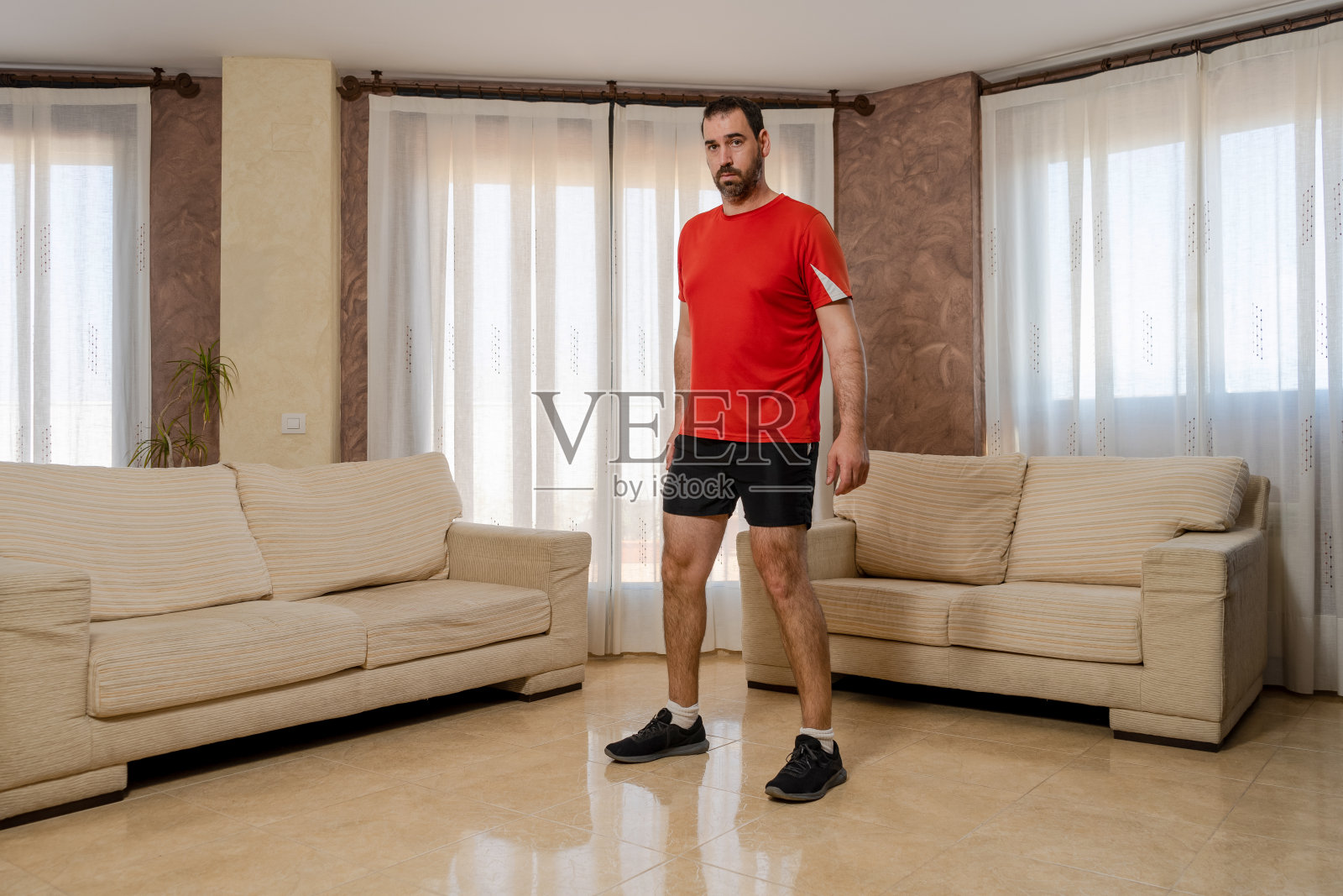 身材健美的大胡子男人穿着运动服在客厅里做深蹲照片摄影图片