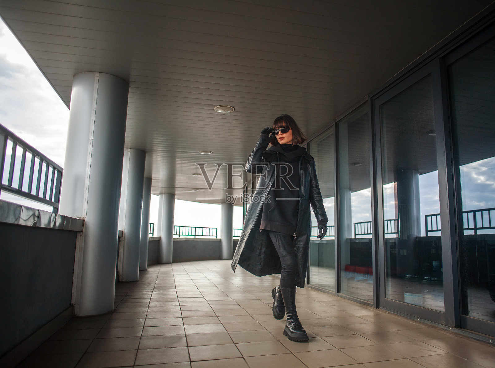 一个穿着黑色皮衣，戴着眼镜的女人匆匆地从商业中心大楼走出来照片摄影图片