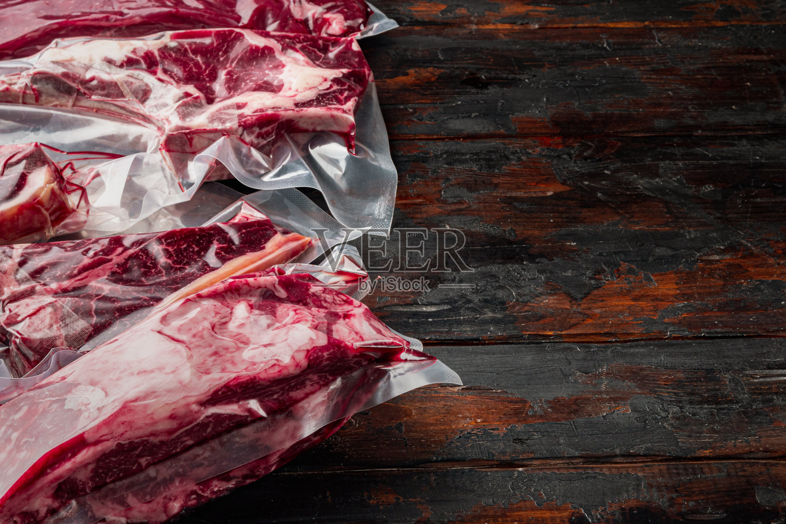 真空包装的有机生牛肉经典切割，烟斗斧，t骨，俱乐部牛排，肋眼和里脊切，在旧的深色木桌子的背景，与文本复制空间照片摄影图片