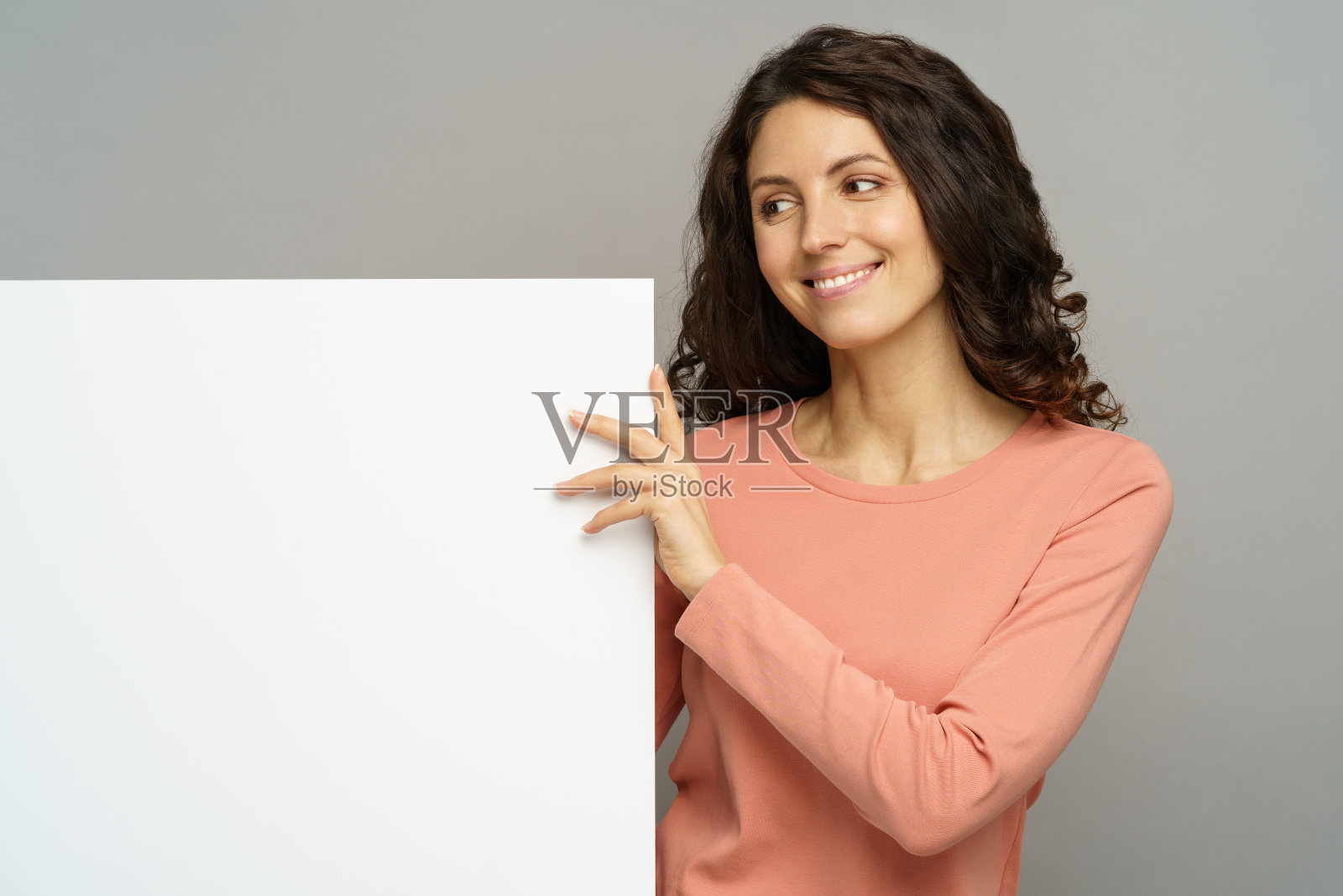 年轻女子手持空白广告牌，面露微笑看向一旁照片摄影图片