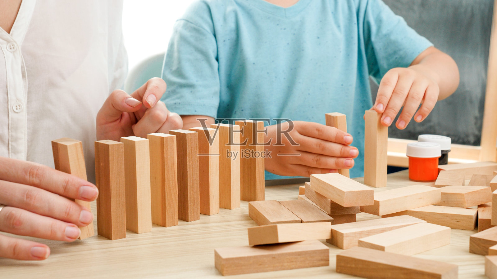 孩子和妈妈玩积木和砖块的特写。多米诺效应或连锁效应。母亲在禁闭和自我隔离期间在家教育和教育她的孩子。家庭的乐趣照片摄影图片