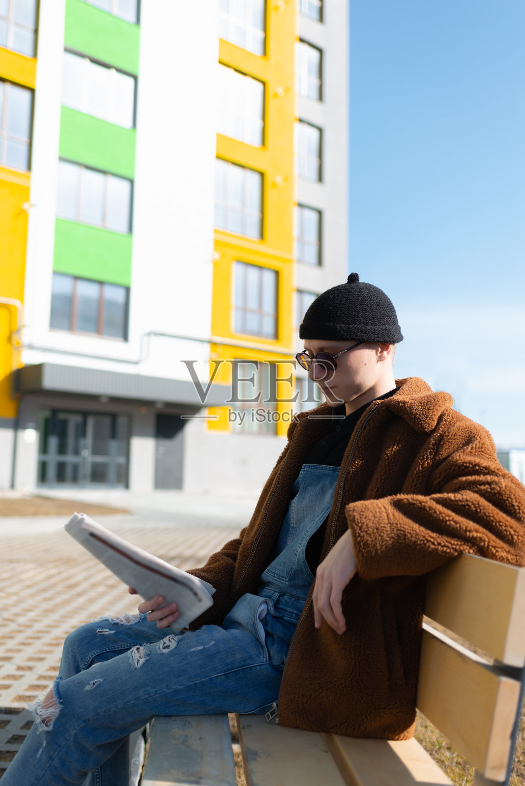 一个男人正坐在一座彩色建筑前的长凳上。阳光明媚的一天。照片摄影图片