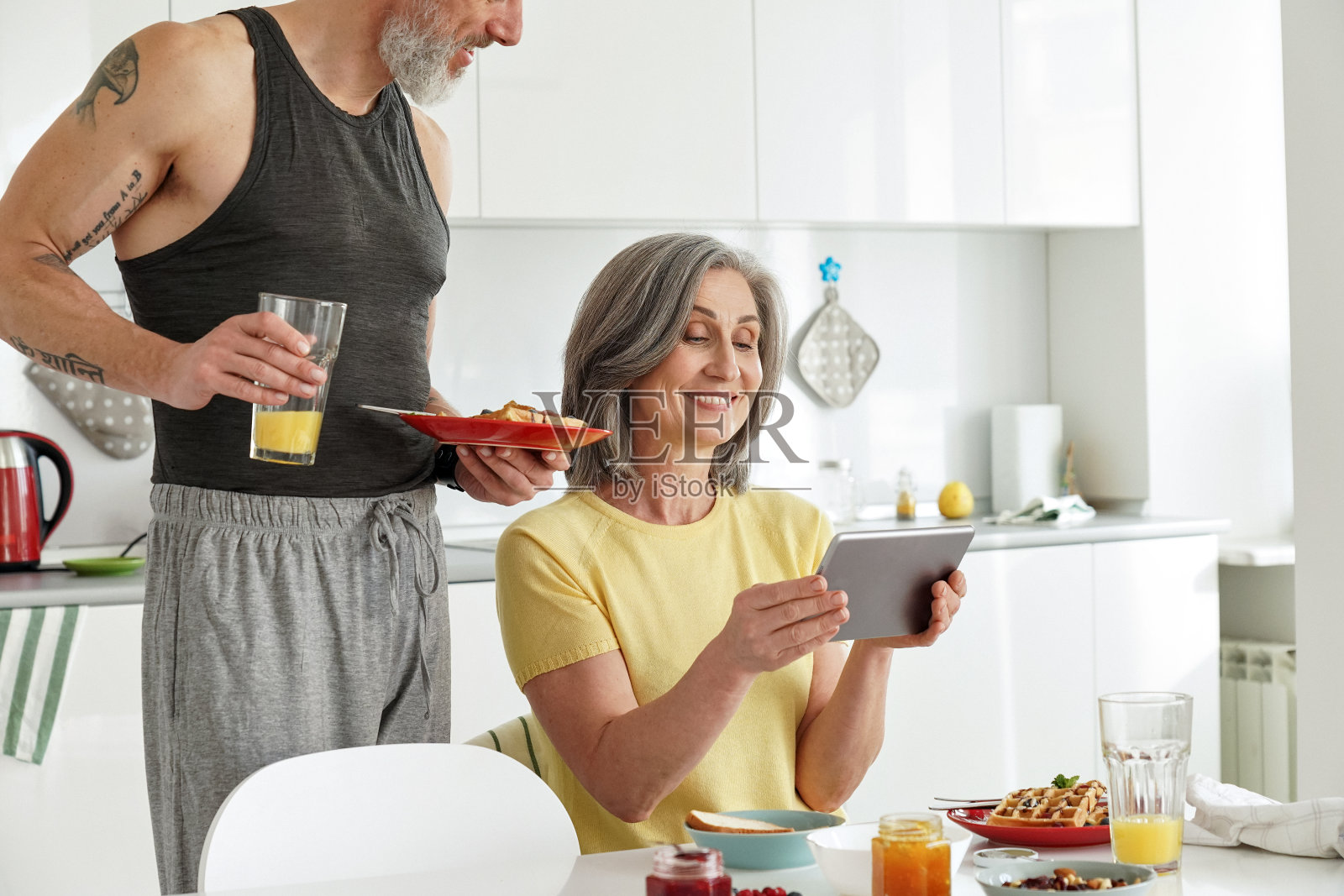幸福的老成熟的家庭夫妇用平板电脑在厨房吃早餐。照片摄影图片