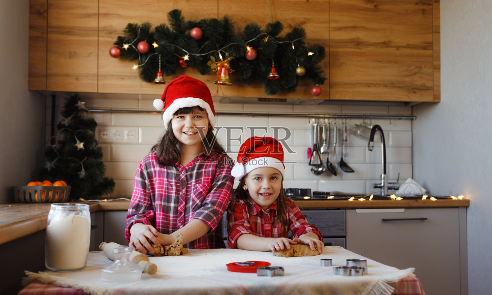 两个十几岁的女孩戴着圣诞帽，正在用生面团做姜饼，开心地笑着照片摄影图片