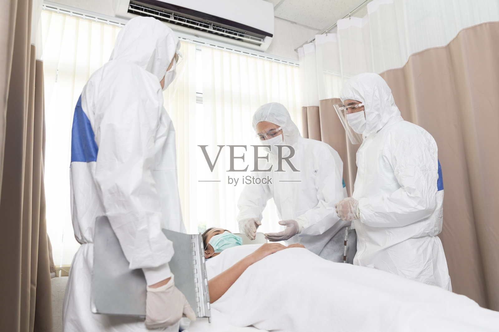 一位亚洲医生正在医院里照顾一位女病人。医生用听诊器分析病人资料。医生为预防COVID - 19在疫区检查患者，实行国家隔离。照片摄影图片