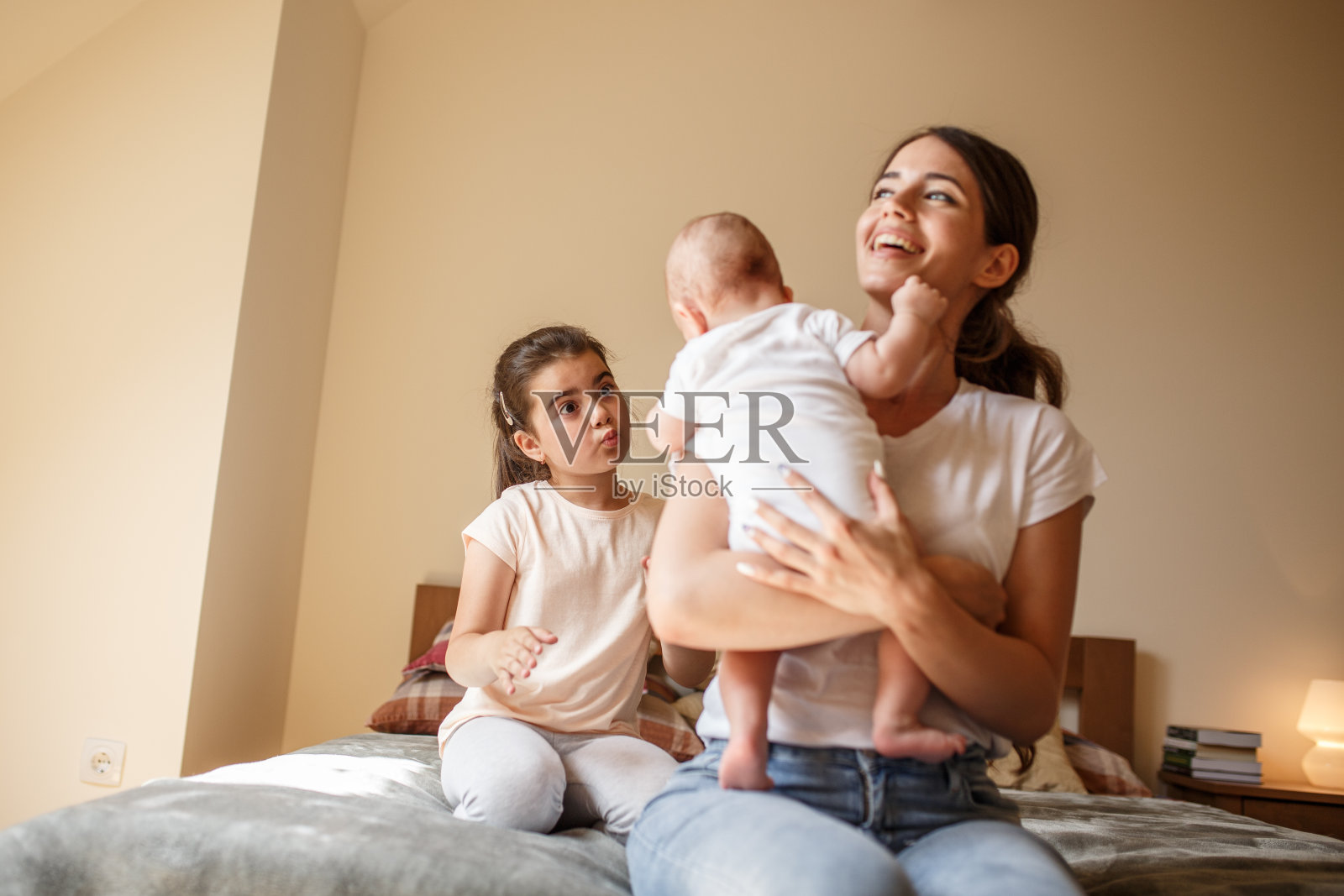 妈妈和她的女儿和男婴在卧室里玩。他们坐在床上开玩笑。照片摄影图片