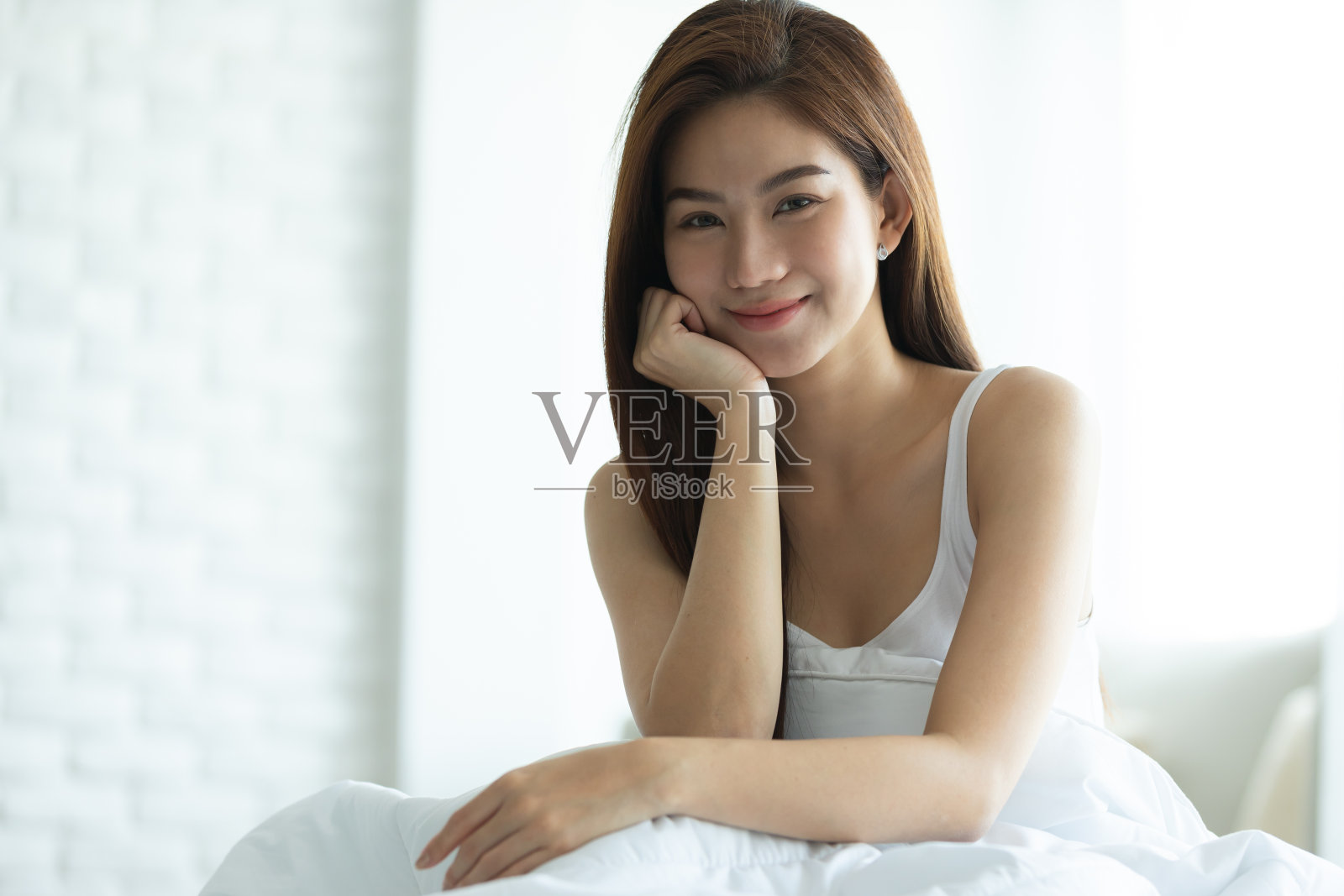 亚洲女人在卧室的白色床上快乐地醒来和微笑。照片摄影图片