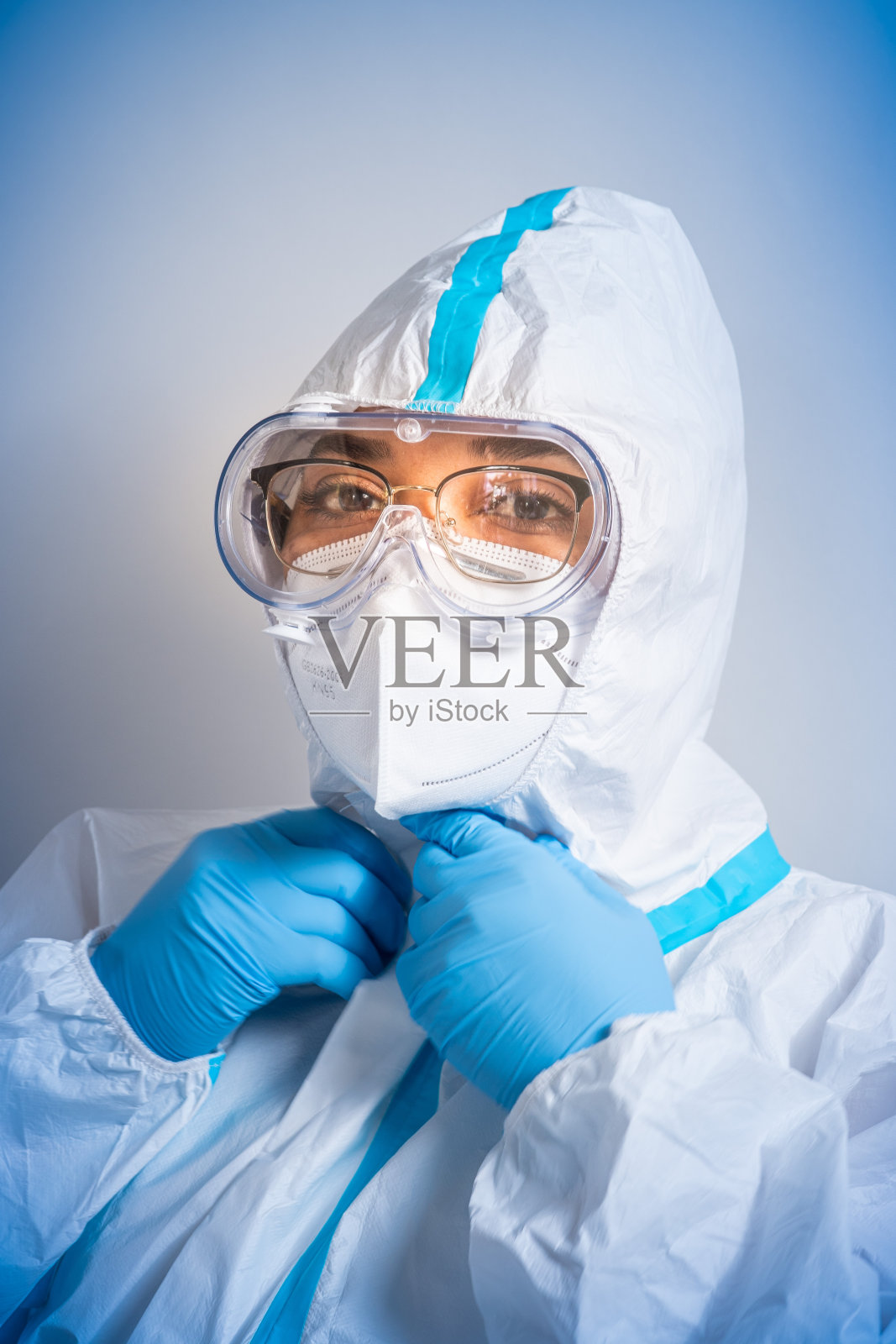 女护士科学家的肖像穿着白色的防护服，医疗防护擦伤眼镜，盾牌和面罩与蓝色手套。冠状病毒大流行covid-19。在医务室接种疫苗。照片摄影图片