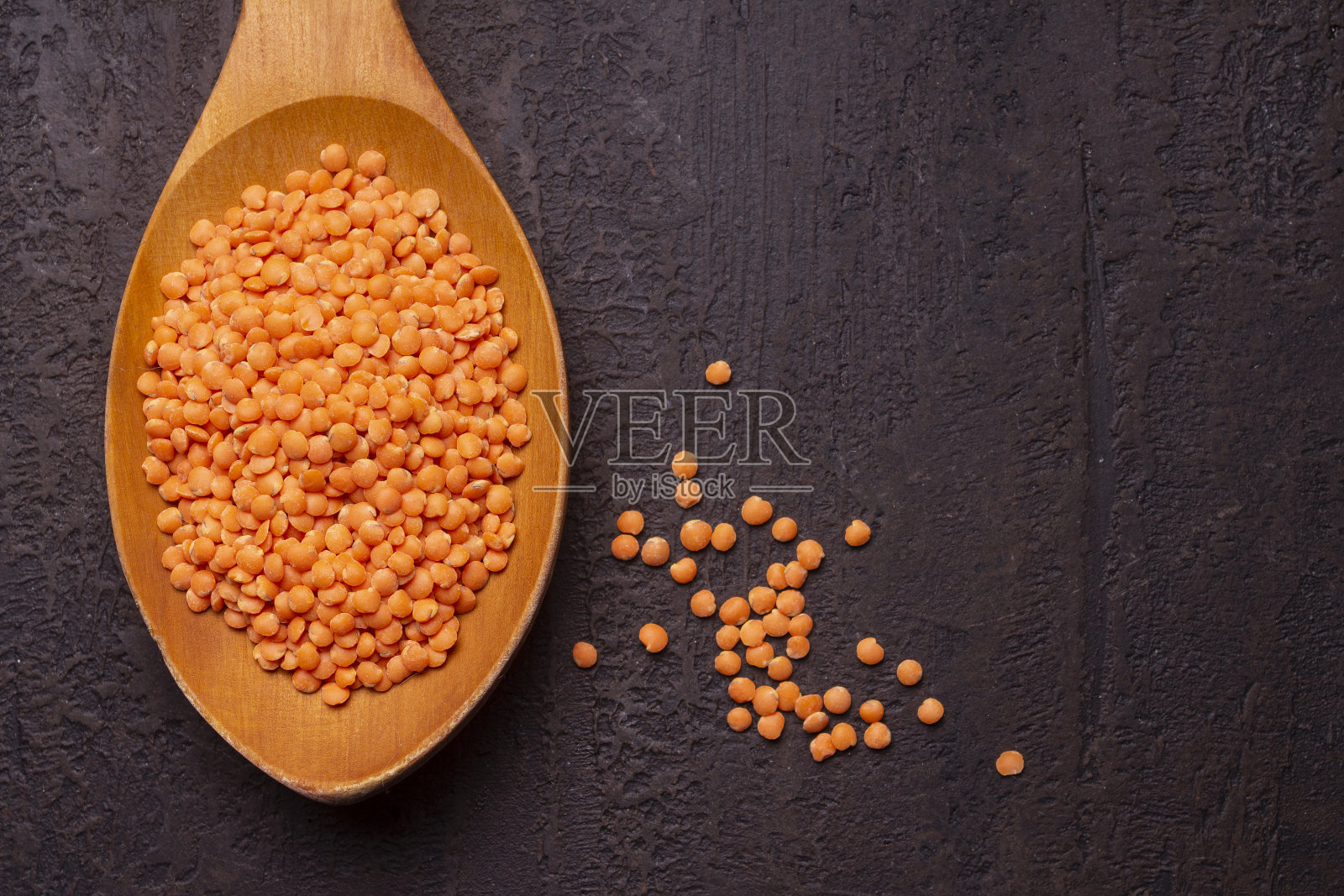 石头桌上的木勺里放着红色的小扁豆。特写镜头。黑暗的照片。照片摄影图片