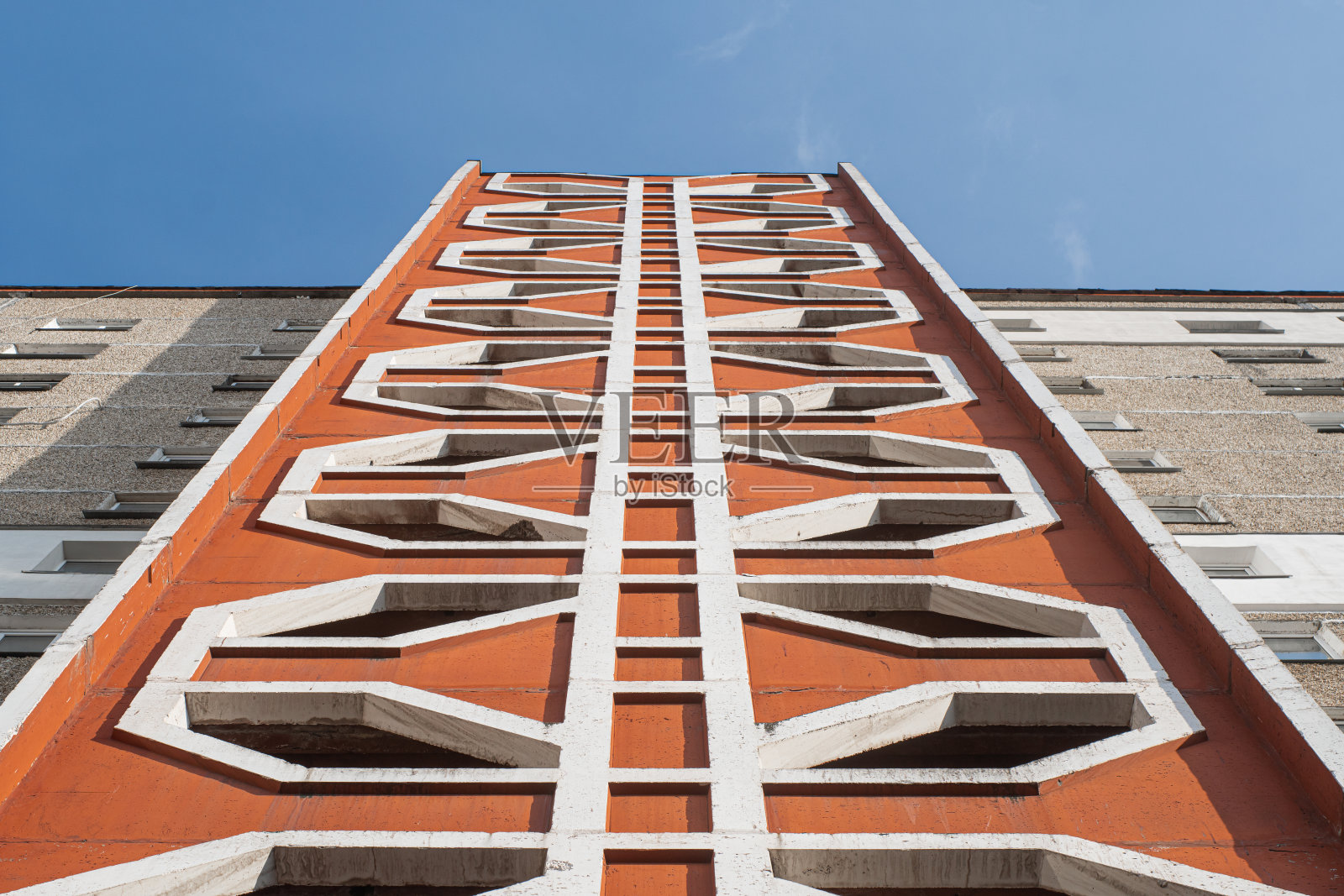 多层混凝土橙色住宅楼与形状的窗户在一个阳光明媚的日子。外观的自底向上视图。照片摄影图片