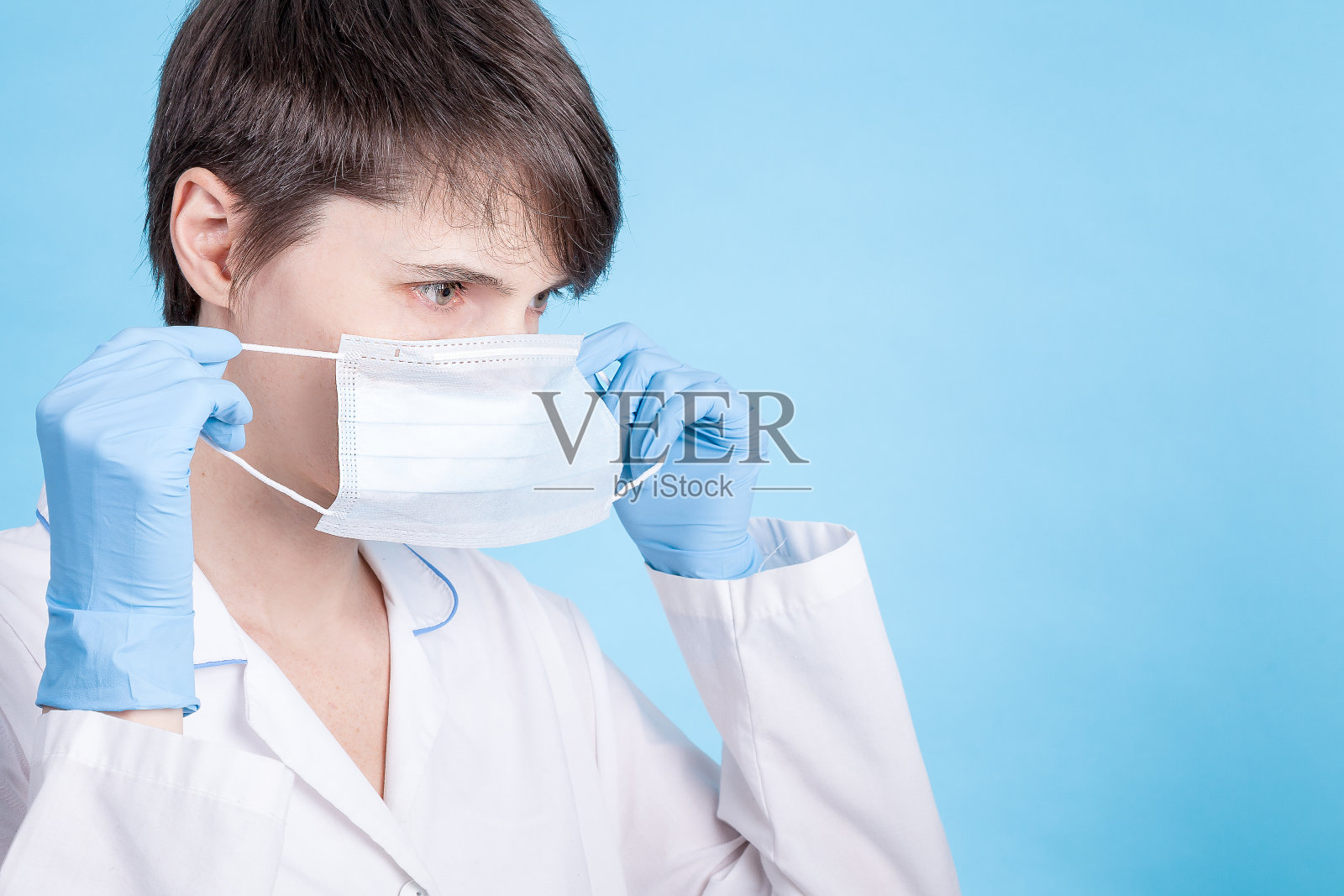 身穿白大褂、戴着蓝手套的医生讲解如何戴口罩。防范COVID-19病毒的概念照片摄影图片