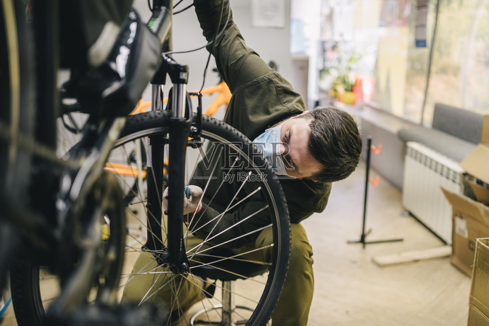 新冠肺炎疫情期间，佩戴防护口罩和手套的自行车修理工按照检疫标准为客户维修自行车车轮。新冠肺炎封锁期间的小企业照片摄影图片