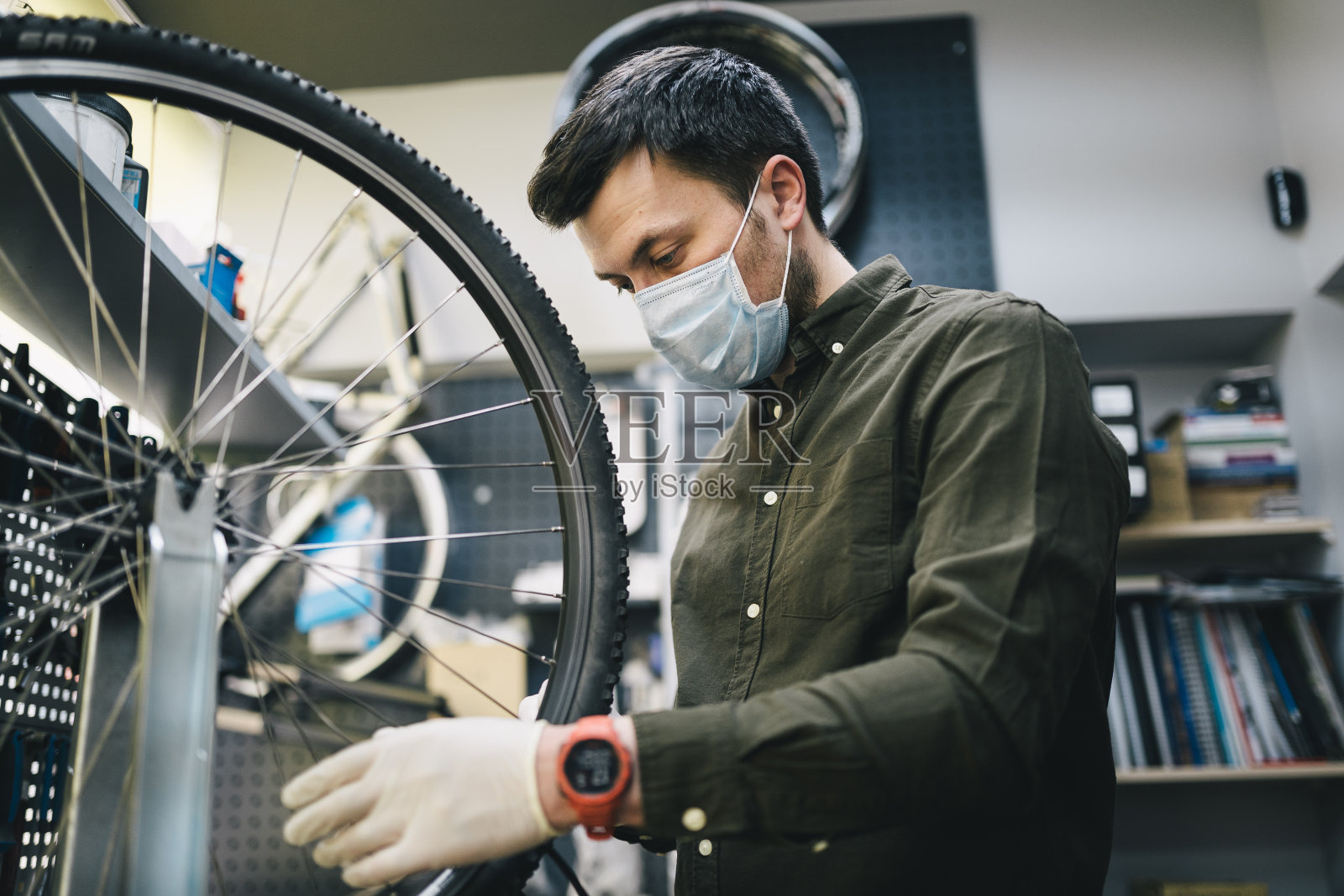 新冠肺炎疫情期间，佩戴防护口罩和手套的自行车修理工按照检疫标准为客户维修自行车车轮。新冠肺炎封锁期间的小企业照片摄影图片