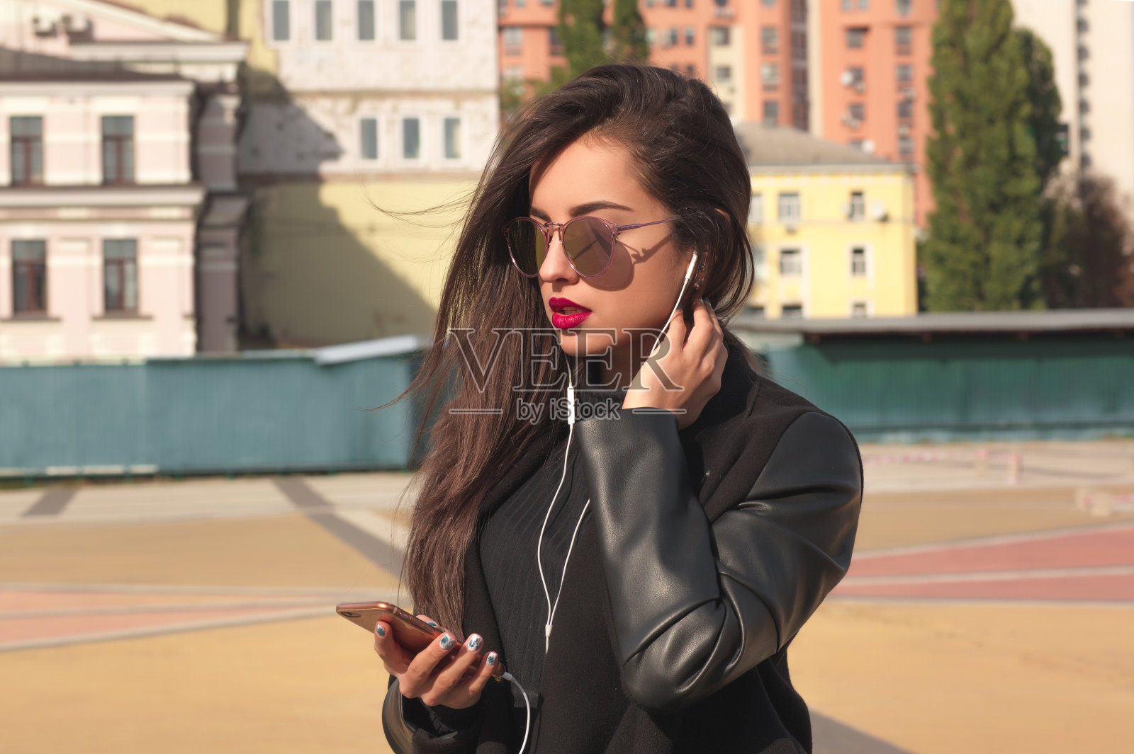 特写的美丽的黑发女人听手机音乐，站在街道上照片摄影图片