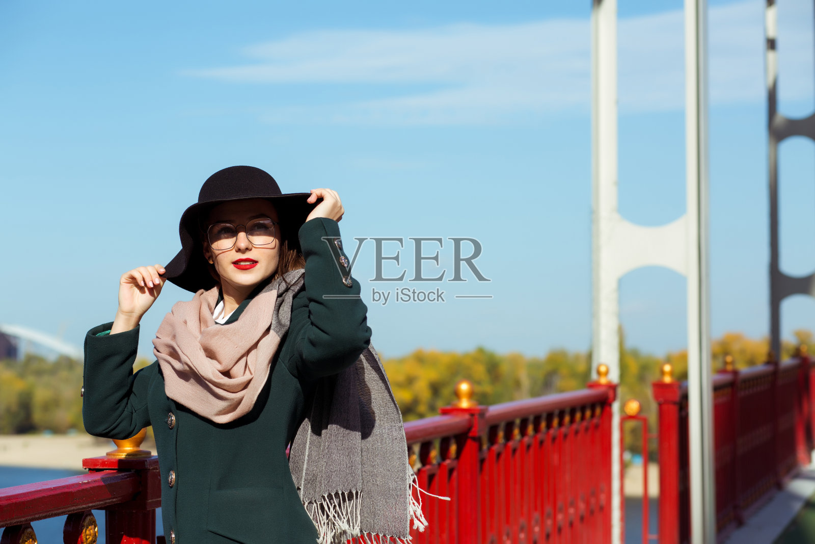 生活方式肖像可爱的年轻模特在桥摆姿势。戴着时髦帽子、围巾和眼镜的女人照片摄影图片