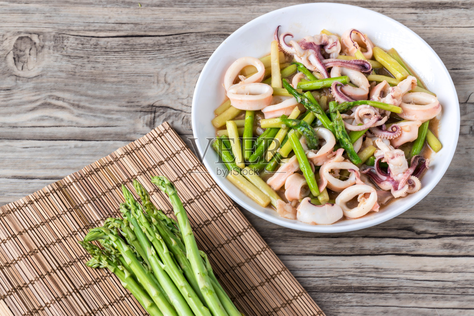 餐厅餐桌上的芦笋炒鱿鱼。木桌白盘炒芦笋。泰国菜，芦笋炒鱿鱼。照片摄影图片