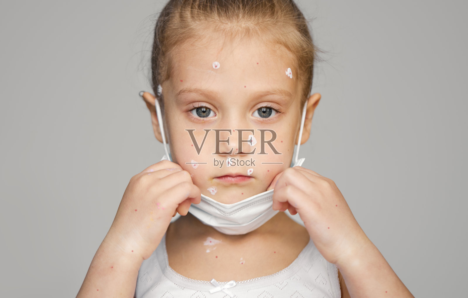 患有水痘的生病的小女孩的肖像，戴着防护口罩。患有水痘病毒或发烧的水痘泡疹的幼儿。手里拿着温度计照片摄影图片