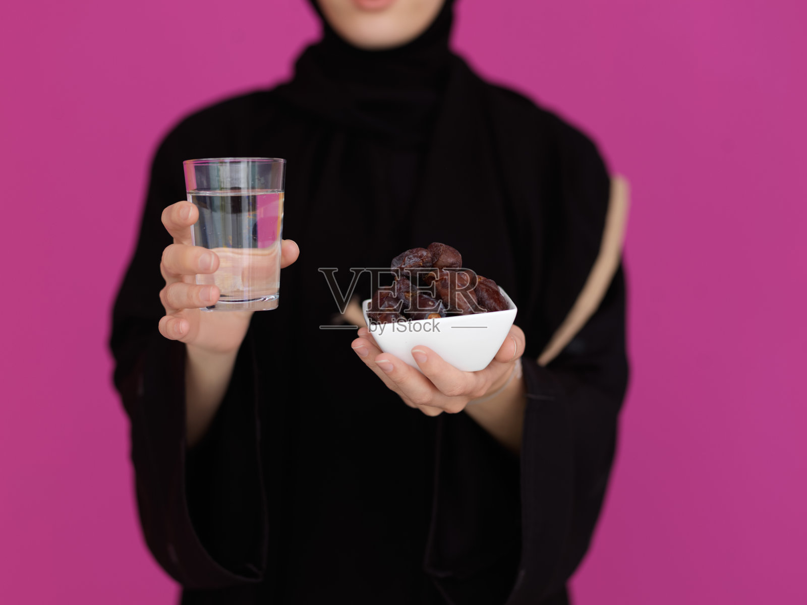 现代穆斯林妇女在阿巴亚举着一个红枣水果和一杯水在她面前照片摄影图片