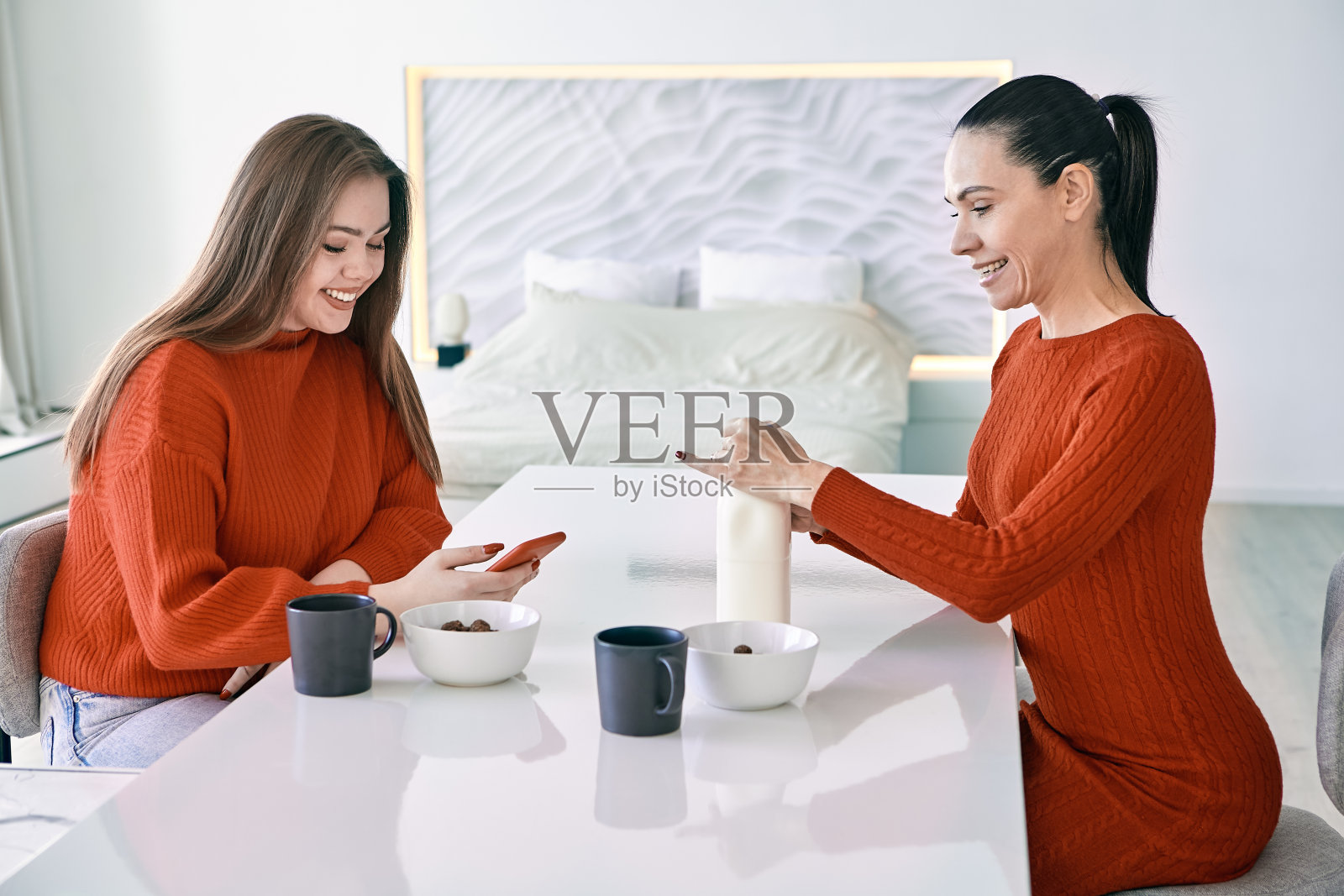 母亲和女儿的家庭早餐，妇女坐在厨房的餐桌上，准备早餐麦片。照片摄影图片