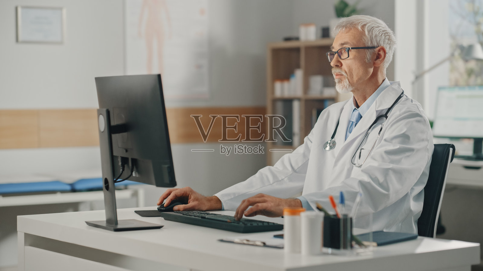 经验丰富的中年男医生穿着白大褂在办公室使用个人电脑。高级医疗保健专业人员处理测试结果，病人治疗计划。照片摄影图片
