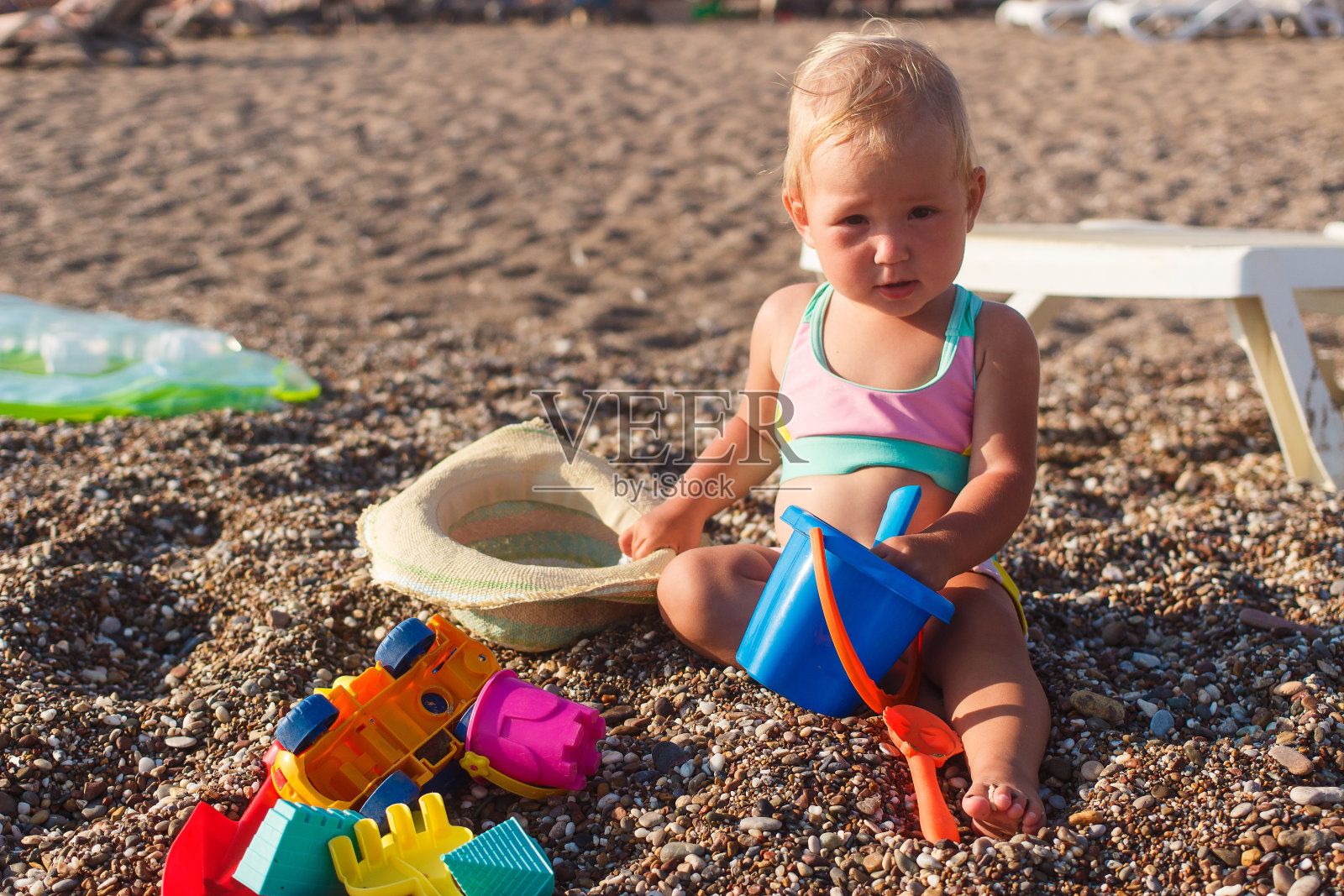金发碧眼的小女孩穿着泳衣坐在沙滩上，在夏天的阳光下玩耍照片摄影图片