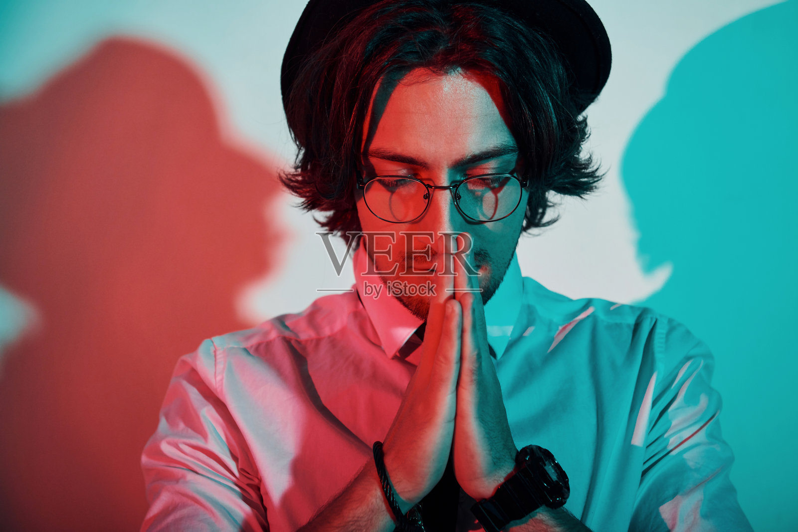 一幅戴着帽子和眼镜的年轻时尚男子的肖像，矗立在工作室的霓虹灯下照片摄影图片