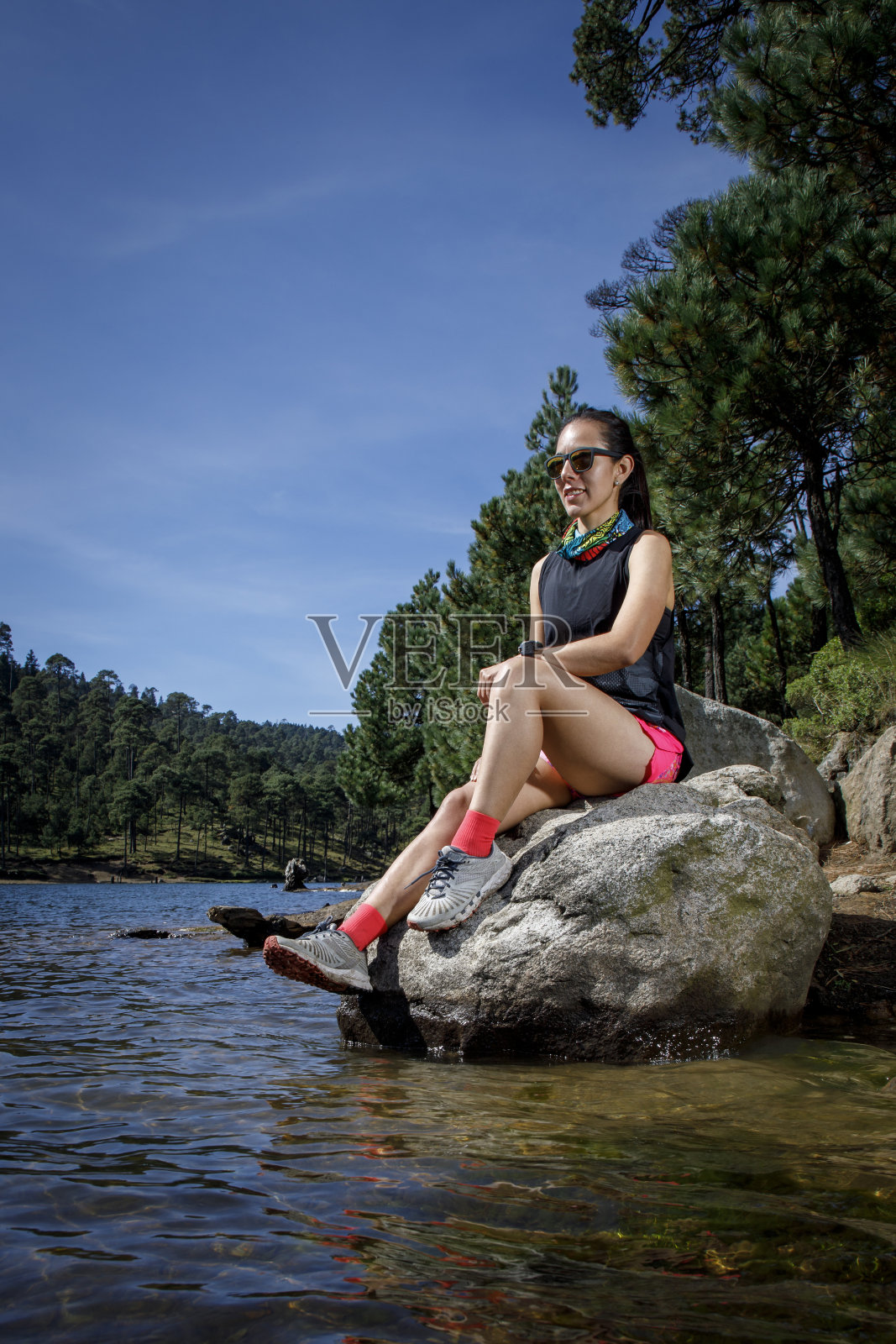 在树林里跑步后，女运动员在湖岸的一块岩石上休息照片摄影图片