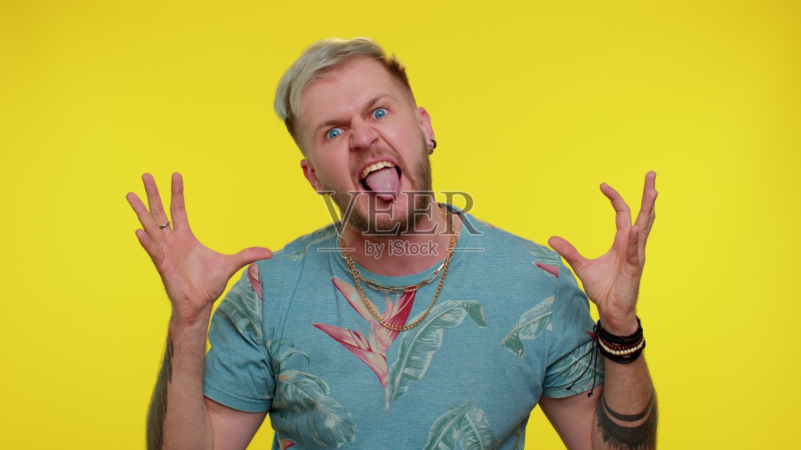 一个疯狂的男人穿着时尚t恤，伸着舌头四处晃悠，做着傻乎乎的鬼脸，非常疯狂照片摄影图片