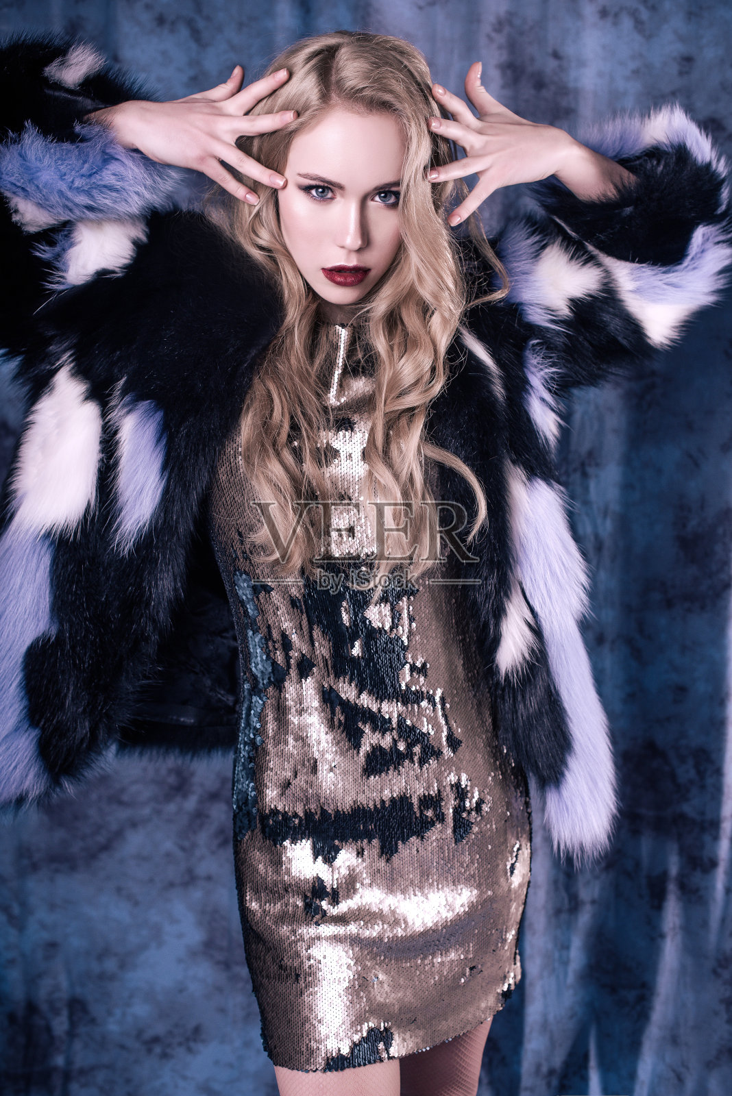 迷人的年轻女子摆姿势在亮片连衣裙和蓝色毛皮大衣。工作室的形象照片摄影图片