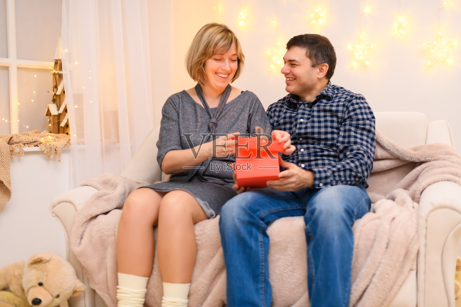 一对浪漫的成年夫妇坐在家里的沙发上，墙上挂着节日灯照片摄影图片