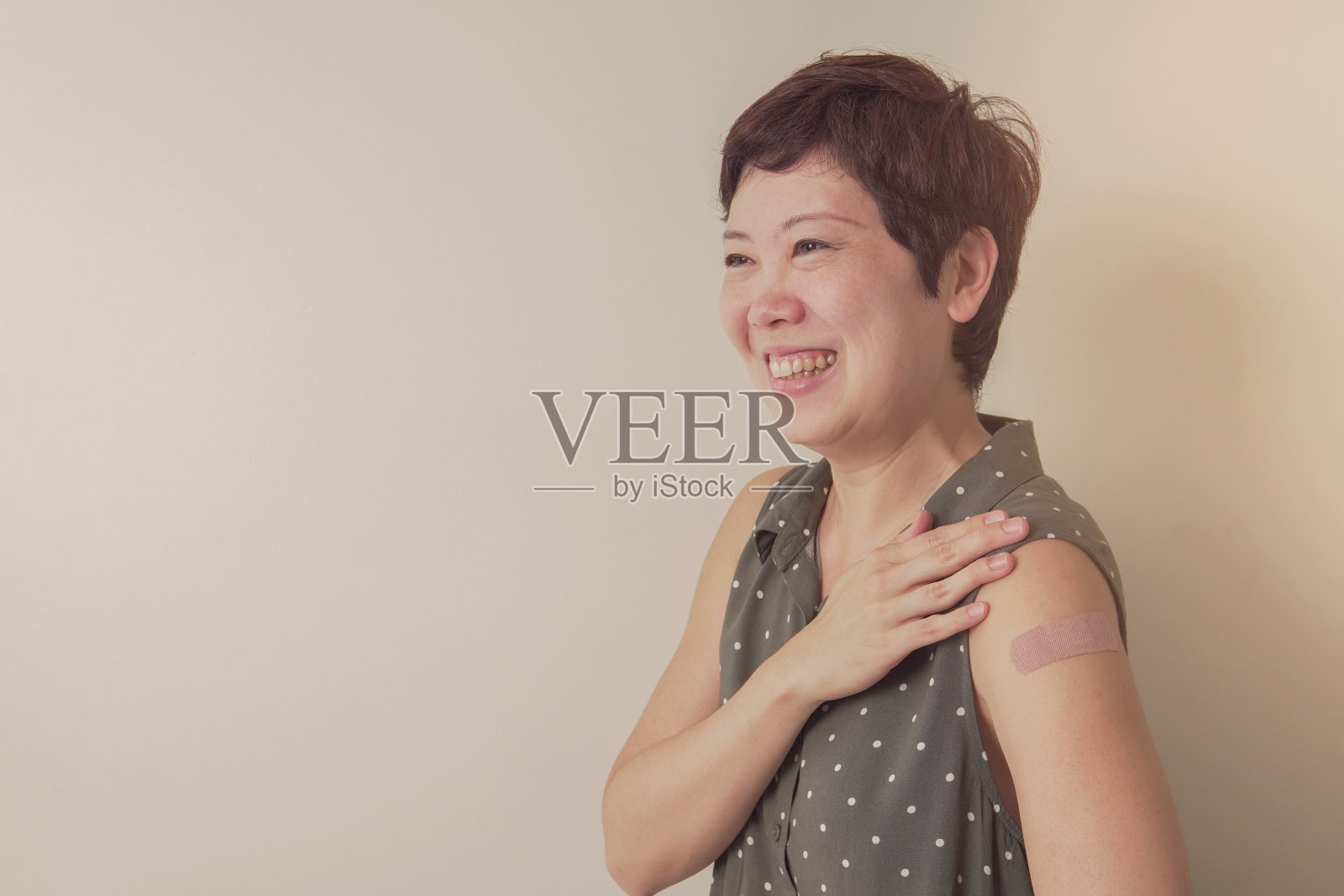 亚洲中年妇女微笑，并显示她的手臂与绷带接种或接种后照片摄影图片