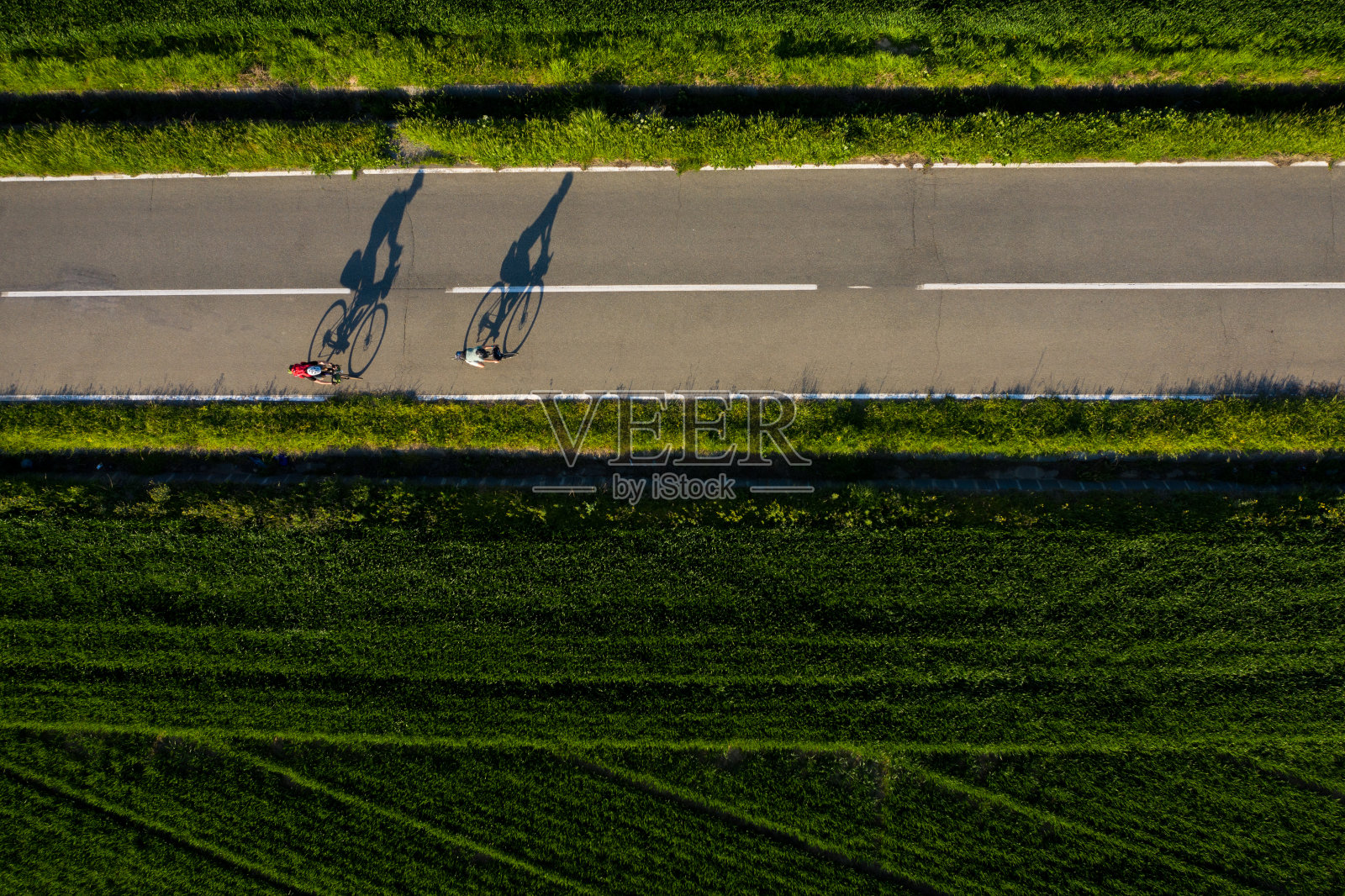 无人机拍摄的两个骑自行车的人和他们的影子投射在日落的道路上照片摄影图片