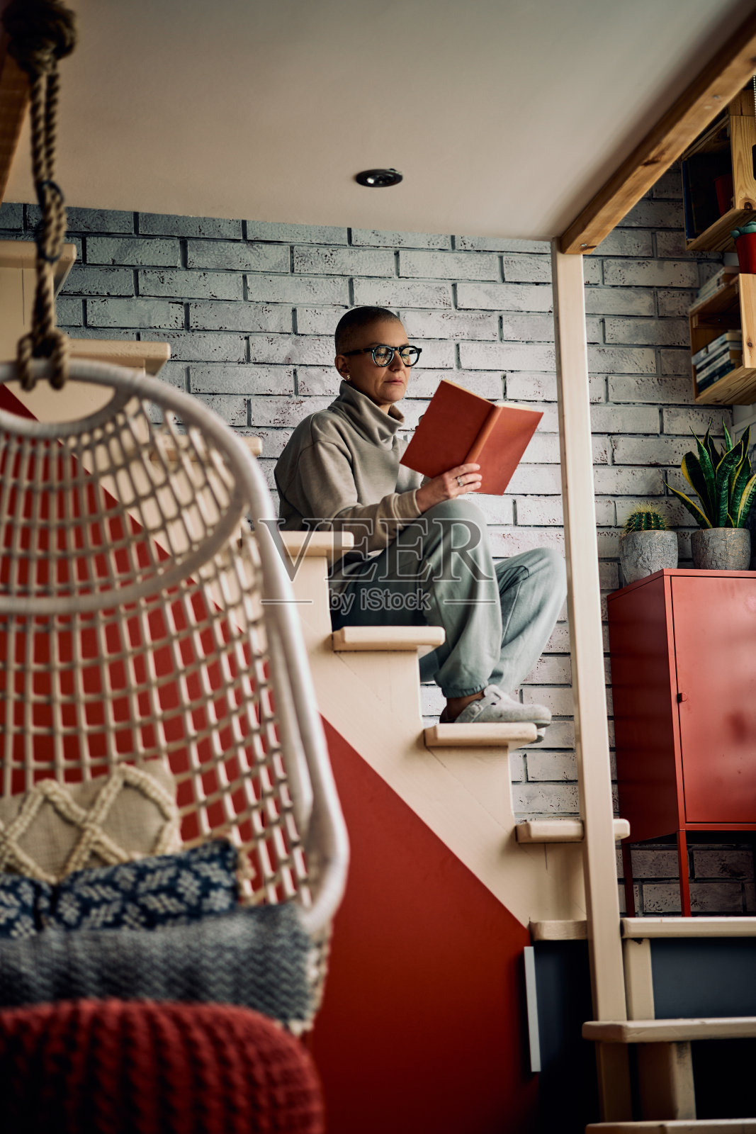 长头发的女人坐在家里的楼梯上读一本有趣的书。照片摄影图片