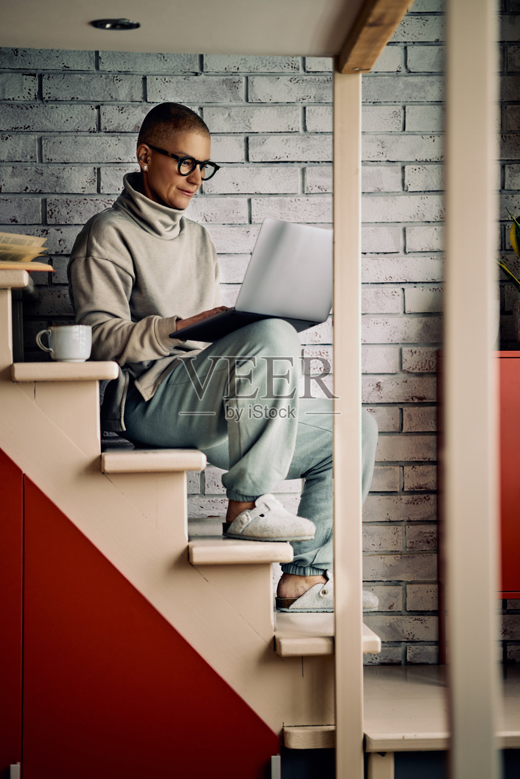 漂亮的资深女士坐在家里的楼梯上用笔记本电脑挂在社交媒体上或工作。照片摄影图片