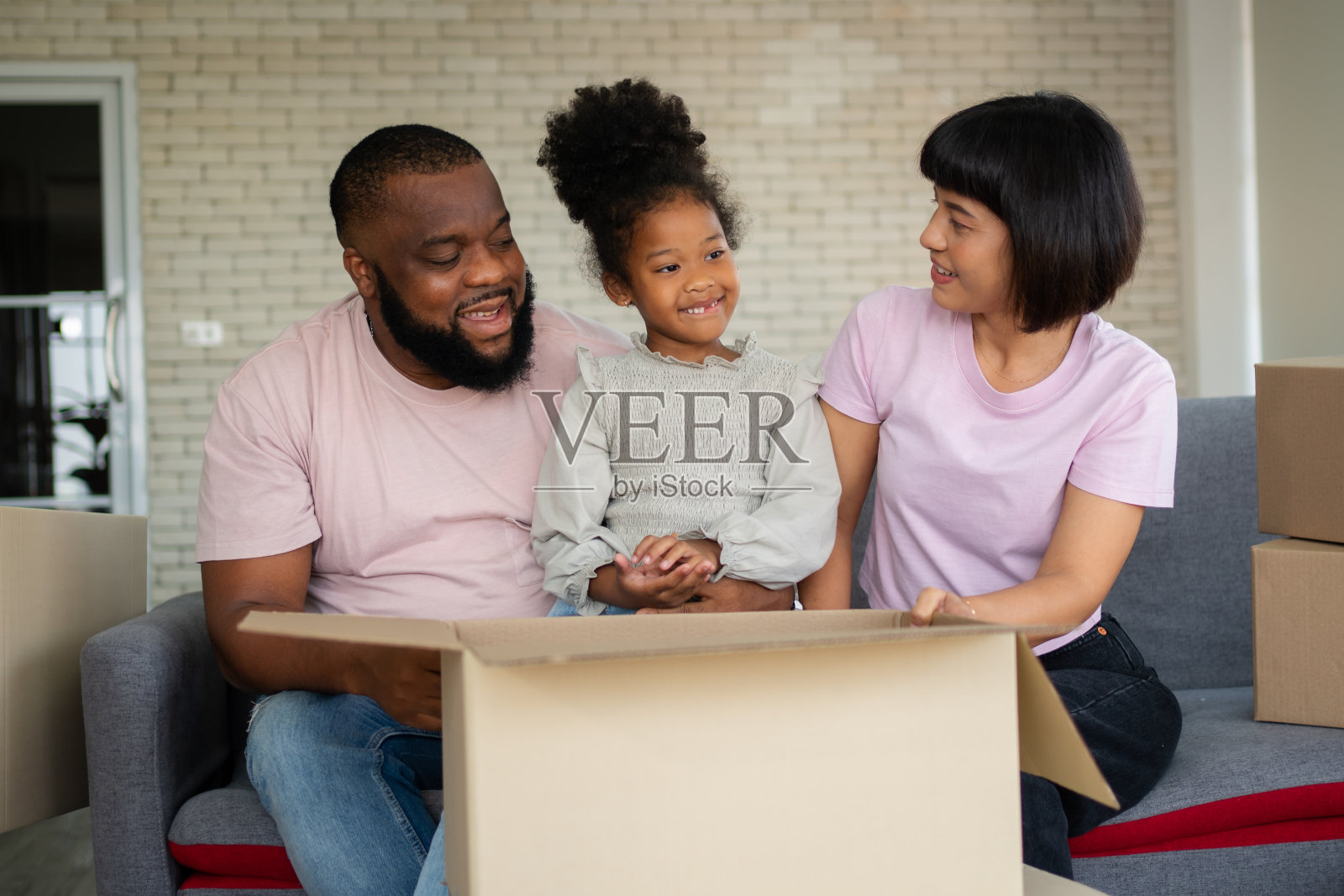 购买房地产的第一天，混血儿家庭搬到新房子后坐在沙发上休息。为新家庭开始新生活的概念。照片摄影图片