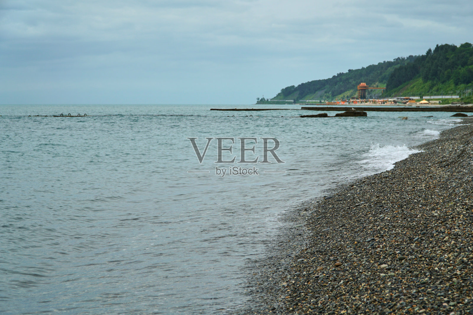 冲浪。海浪拍打着石滩。寒冷的海边。灰色的天空和海洋。照片摄影图片