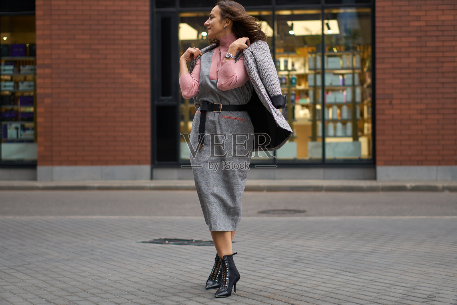 一个穿着灰色连衣裙的女人走在街上。办公室的风格。时尚的头发。照片摄影图片