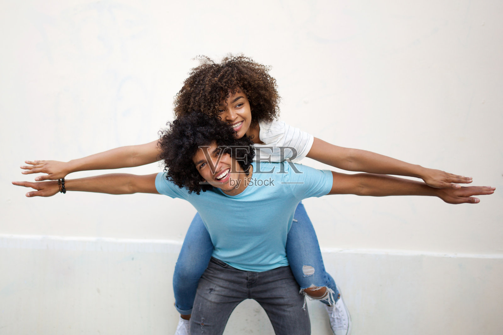 一个年轻的黑人男人背着一个快乐的非洲裔美国女人，伸开双臂做飞机照片摄影图片