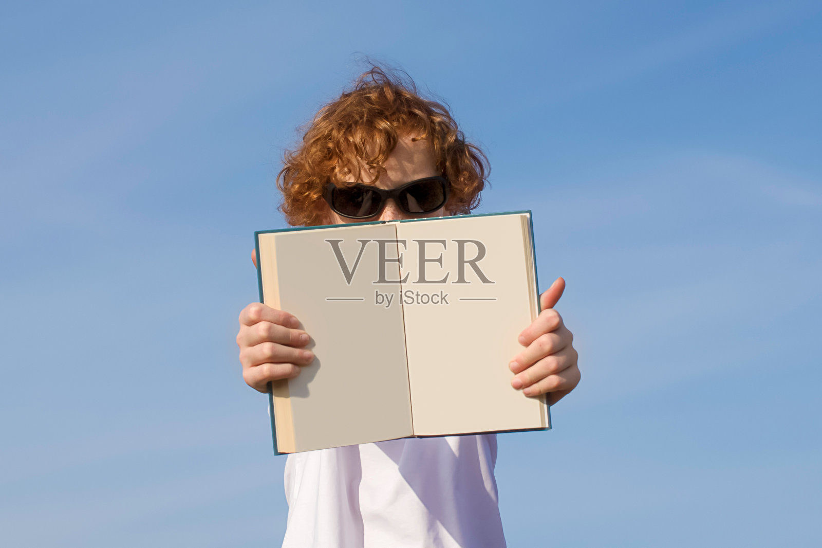 副本的空间。12-14岁的男孩戴着太阳镜，手里拿着一本打开的空白书照片摄影图片