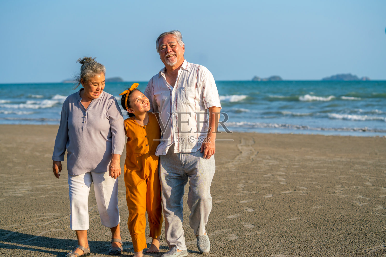 阳光明媚的日子里，祖父母和孙女一起在海滩上散步照片摄影图片