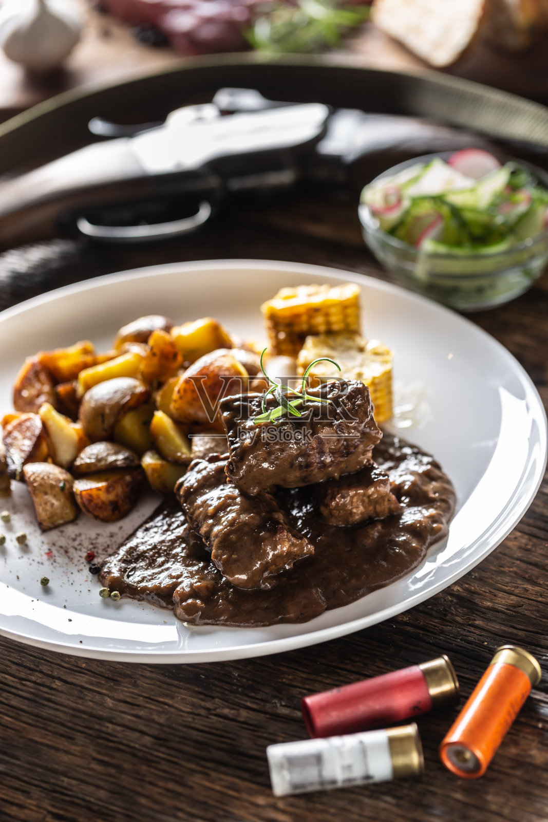 野味炖牛肉配烤土豆，用四色胡椒玉米调味。天然食品被猎枪和子弹包围着。照片摄影图片
