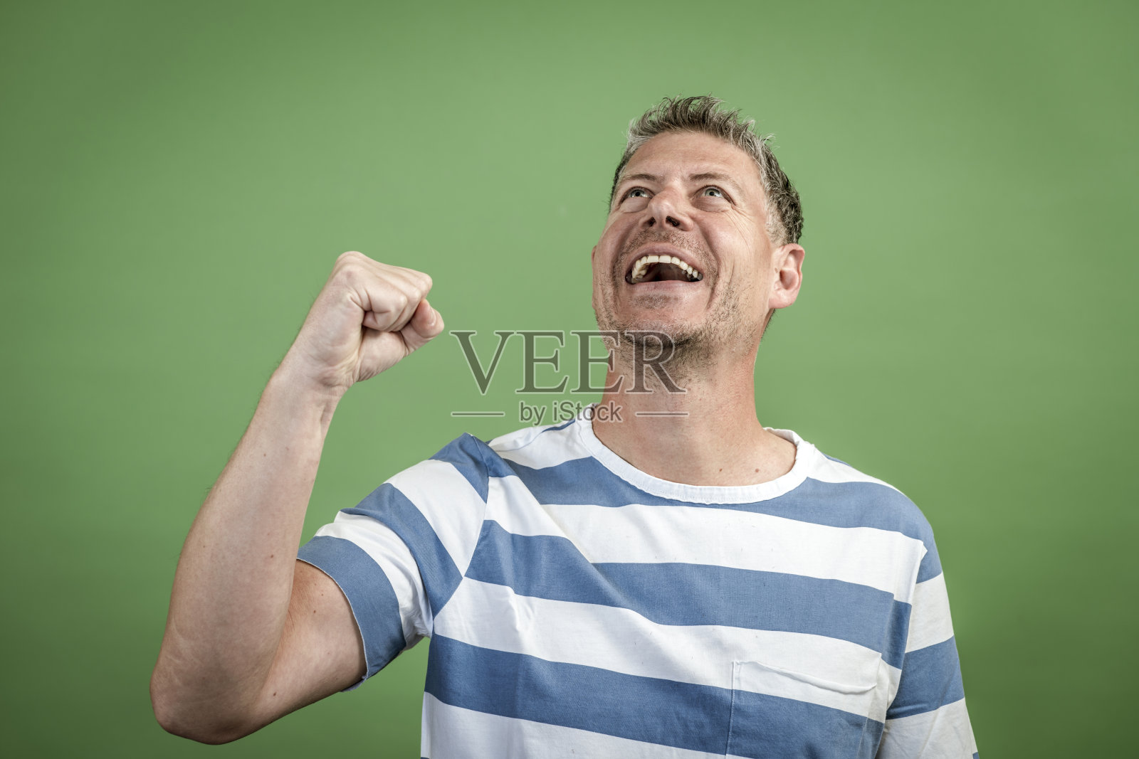 一个40岁出头的男人，灰白头发，三天胡子，白色蓝条纹t恤在绿色背景前摆姿势照片摄影图片