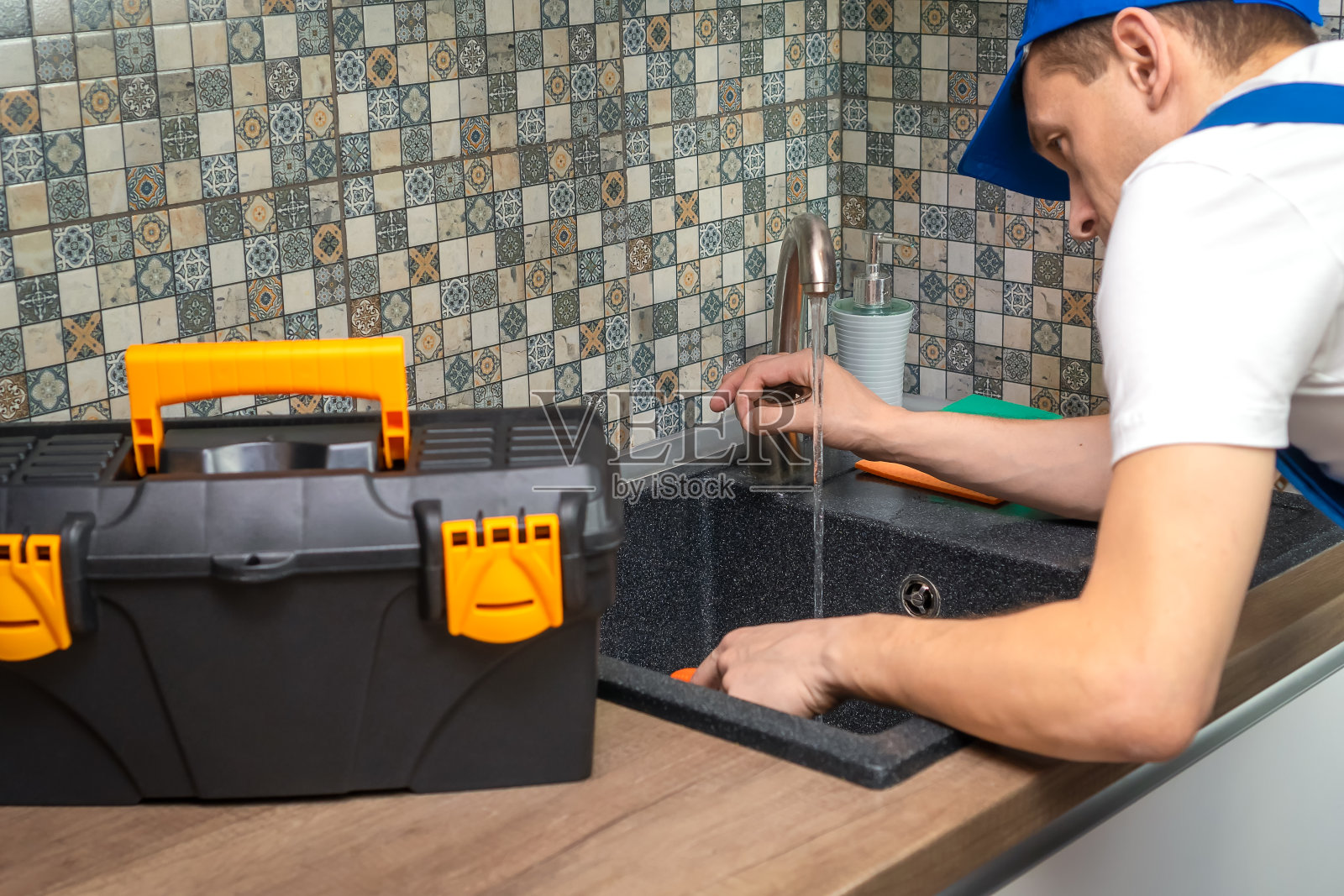 修理工在专门检查衣服、修理水龙头的现代厨房里，旁边有一箱工具。水龙头包括照片摄影图片