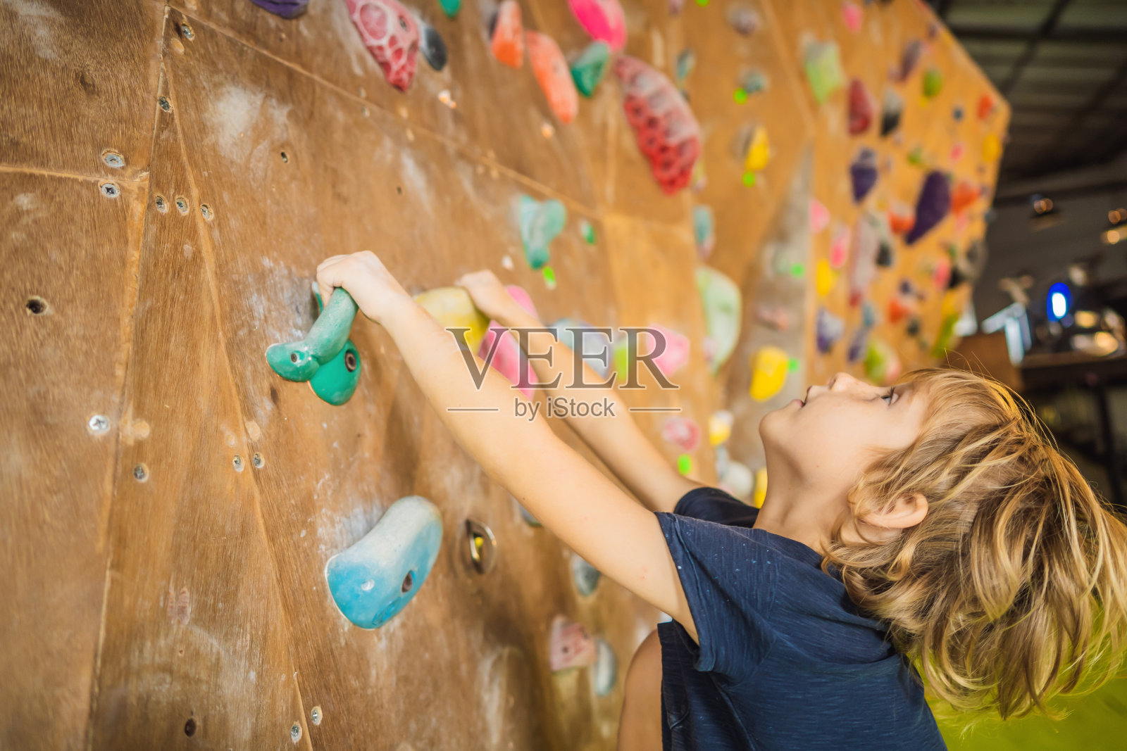 小男孩穿着特制的靴子在爬岩壁。室内照片摄影图片