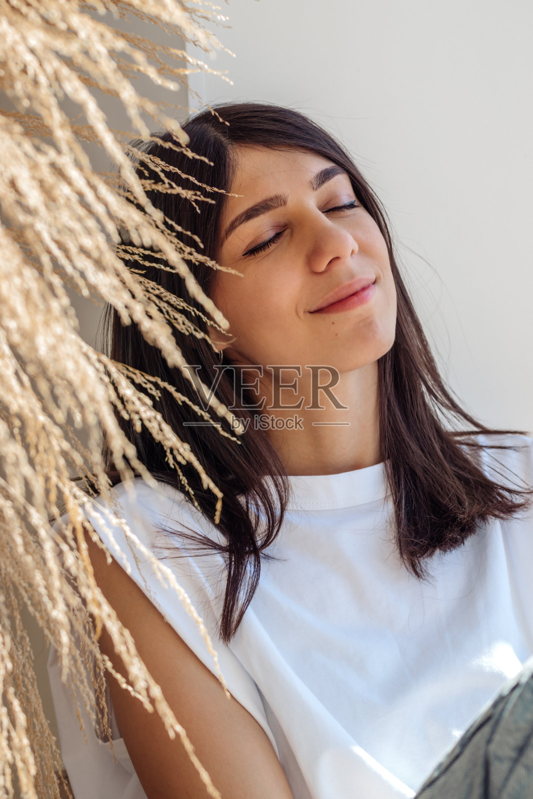 一个黑发混血女孩坐在窗台上，享受着阳光明媚的日子。家庭室内设计。窗外的城市景色。放松和好心情的概念照片摄影图片