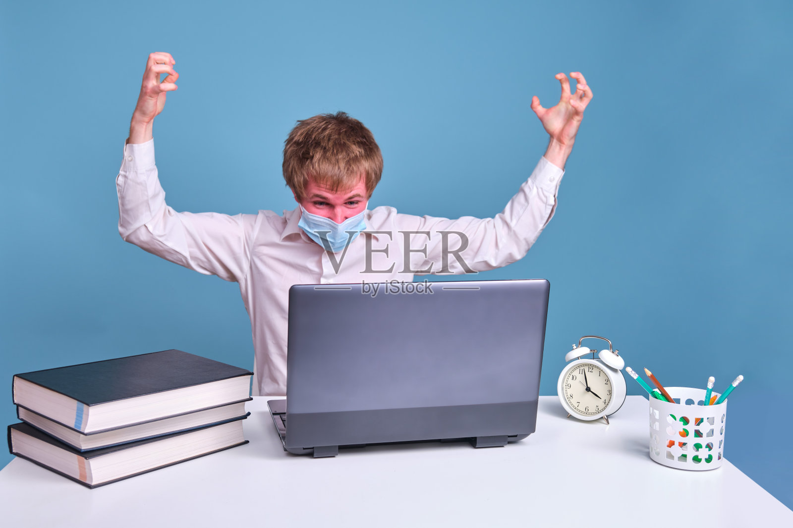 愤怒的人在医疗面罩工作在笔记本电脑后面的蓝色工作室背景照片摄影图片